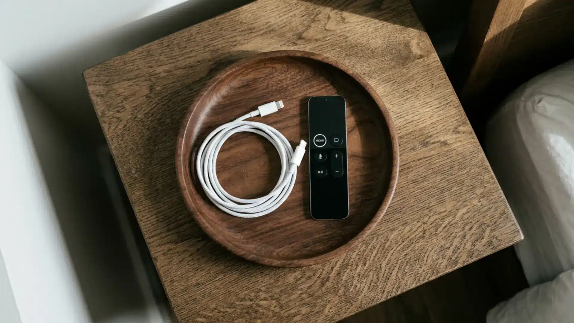 overhead view of small wooden tray on nightstand holding coiled charging cable and remote