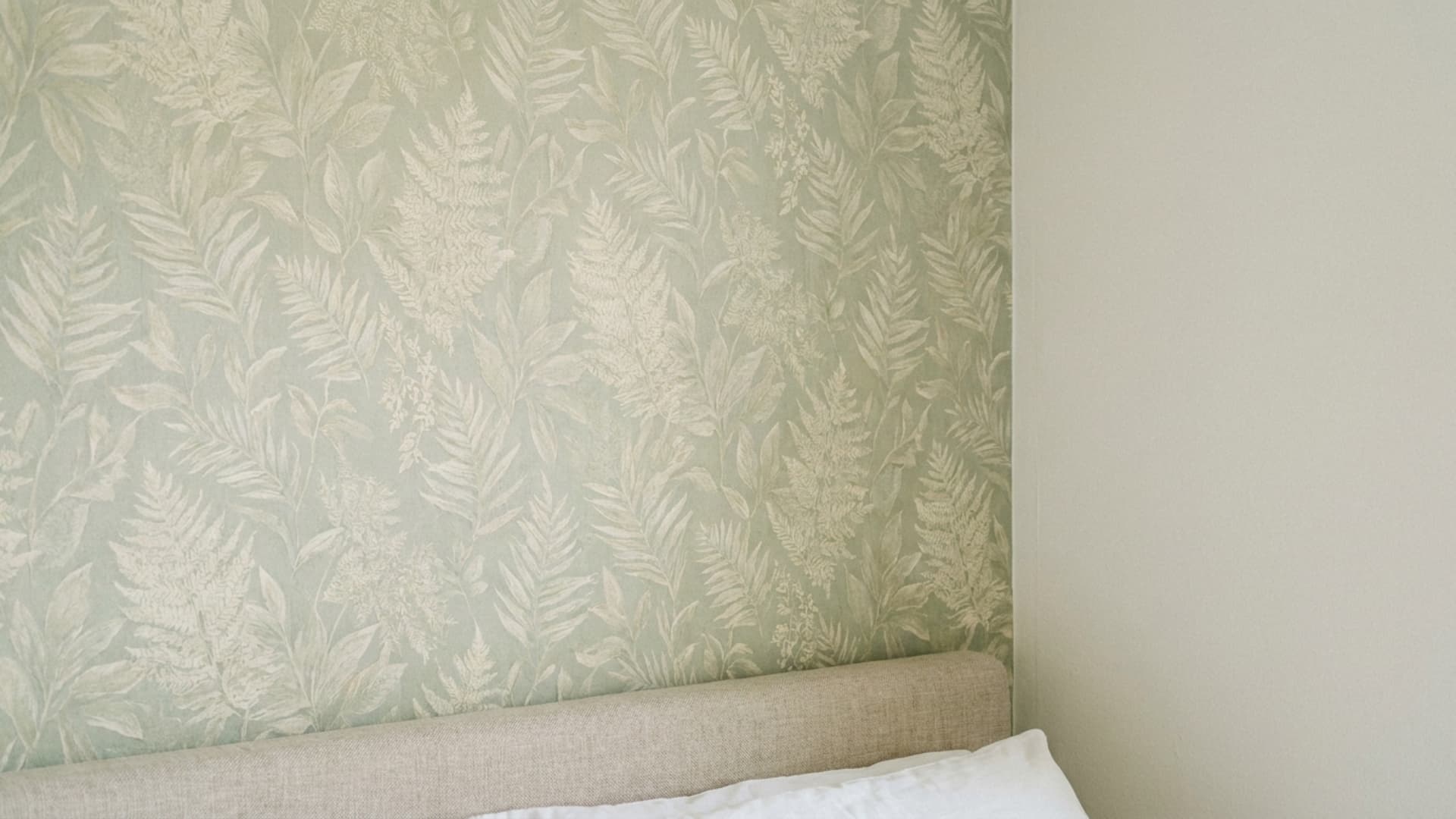 subtle botanical peel-and-stick wallpaper behind a guest bed headboard and white pillow