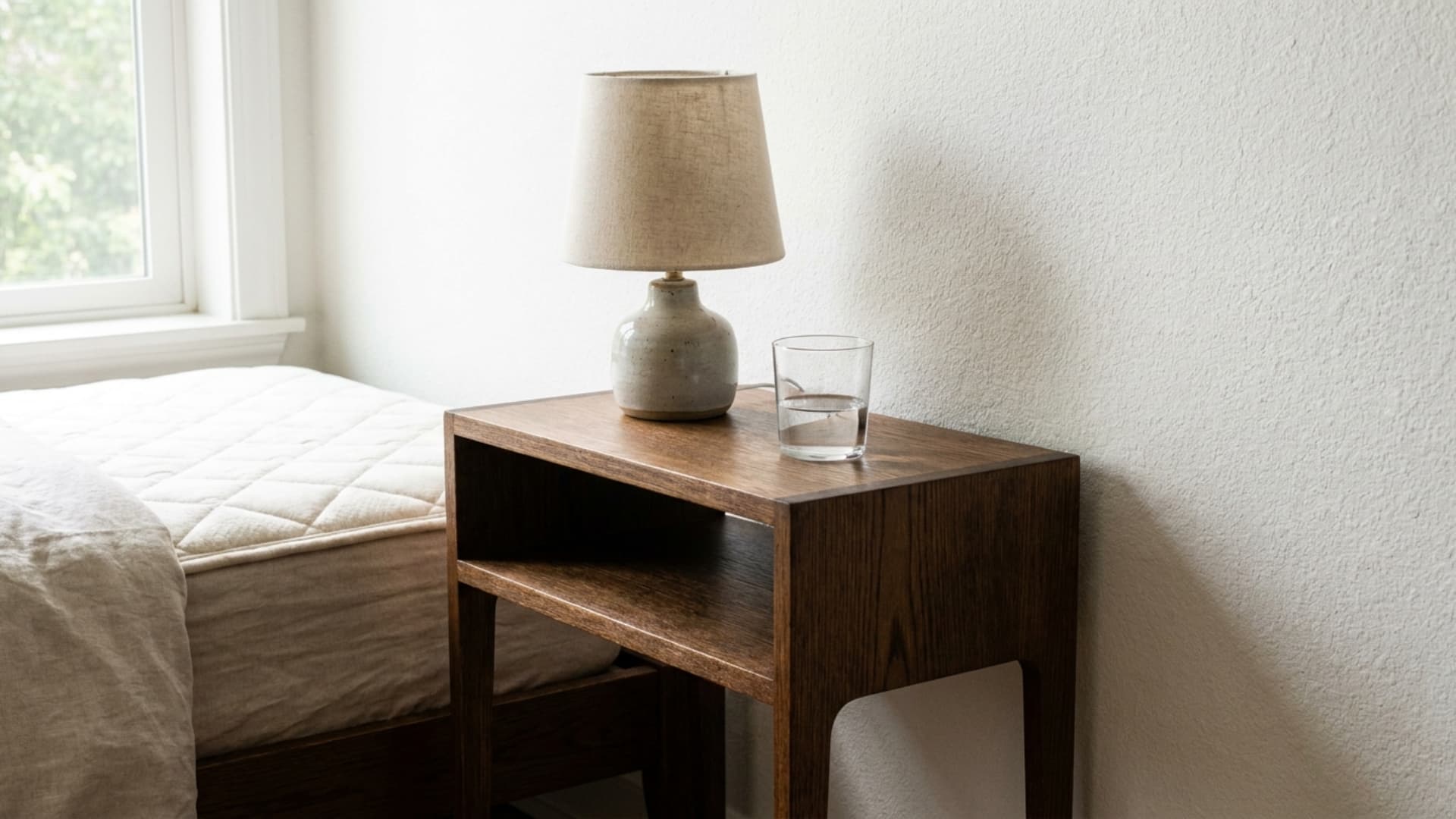 two matching slim wooden nightstands flanking a neatly made white guest bed