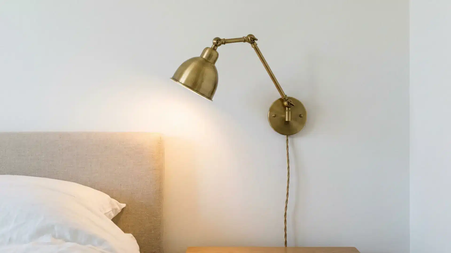 plug-in wall sconce at reading height on white wall beside guest bed with clear nightstand