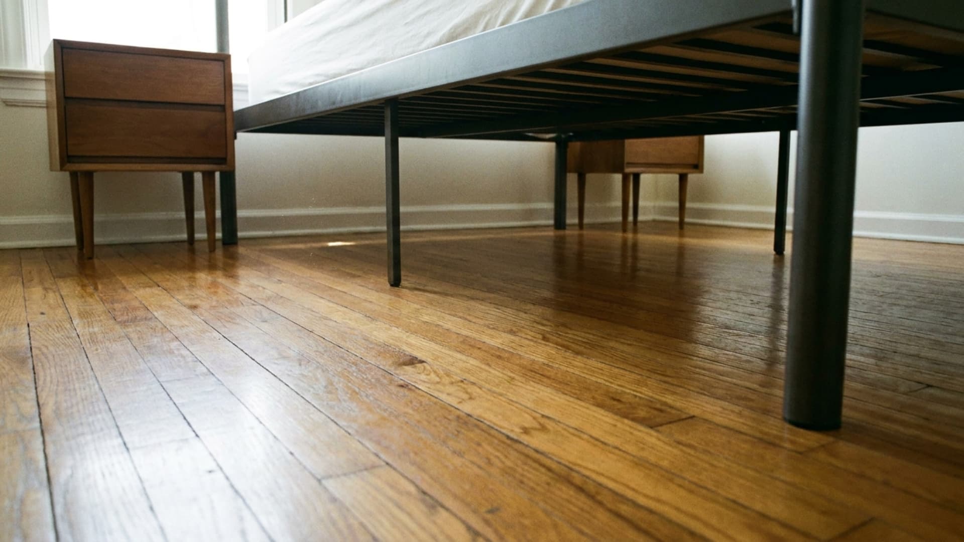 floor-level view beneath guest bed frame and nightstands with slim legs on hardwood floor