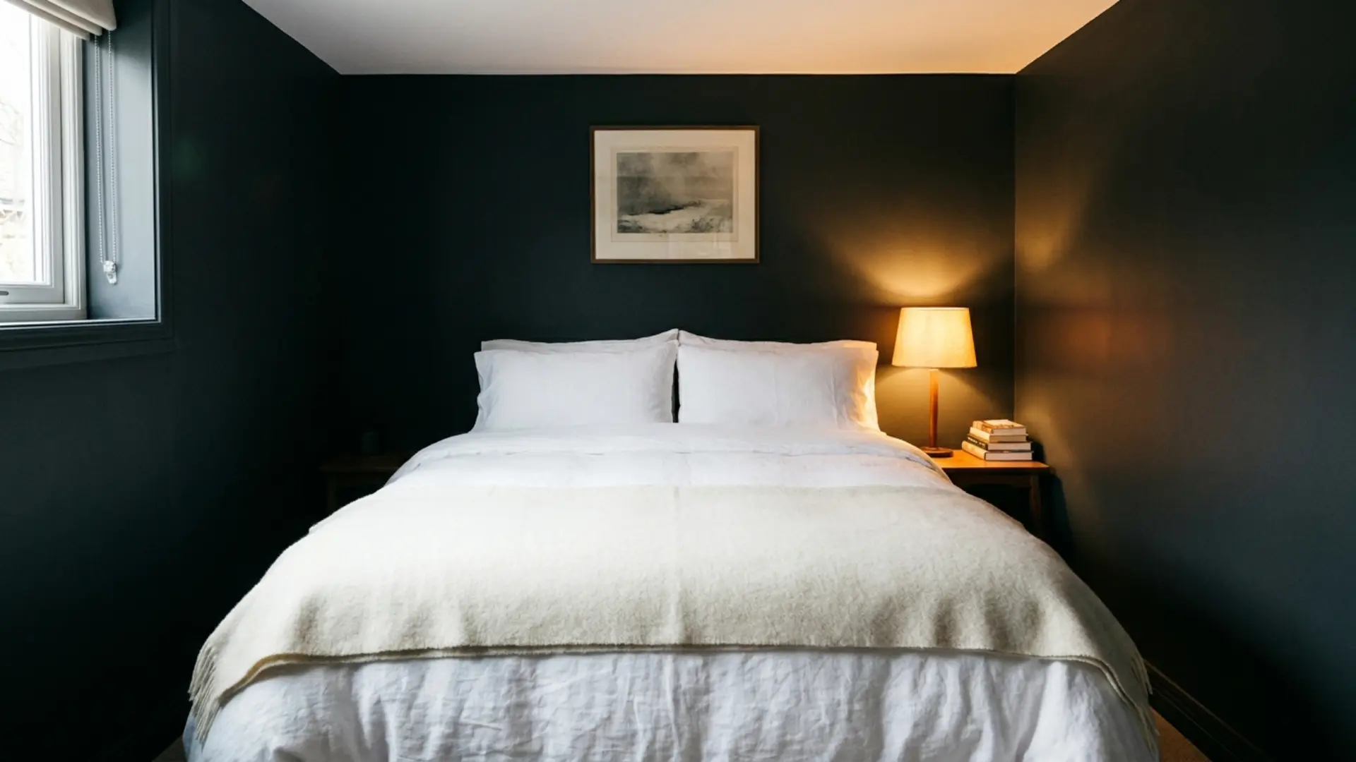 narrow guest room with charcoal walls, white bedding, and warm bedside lamp glow