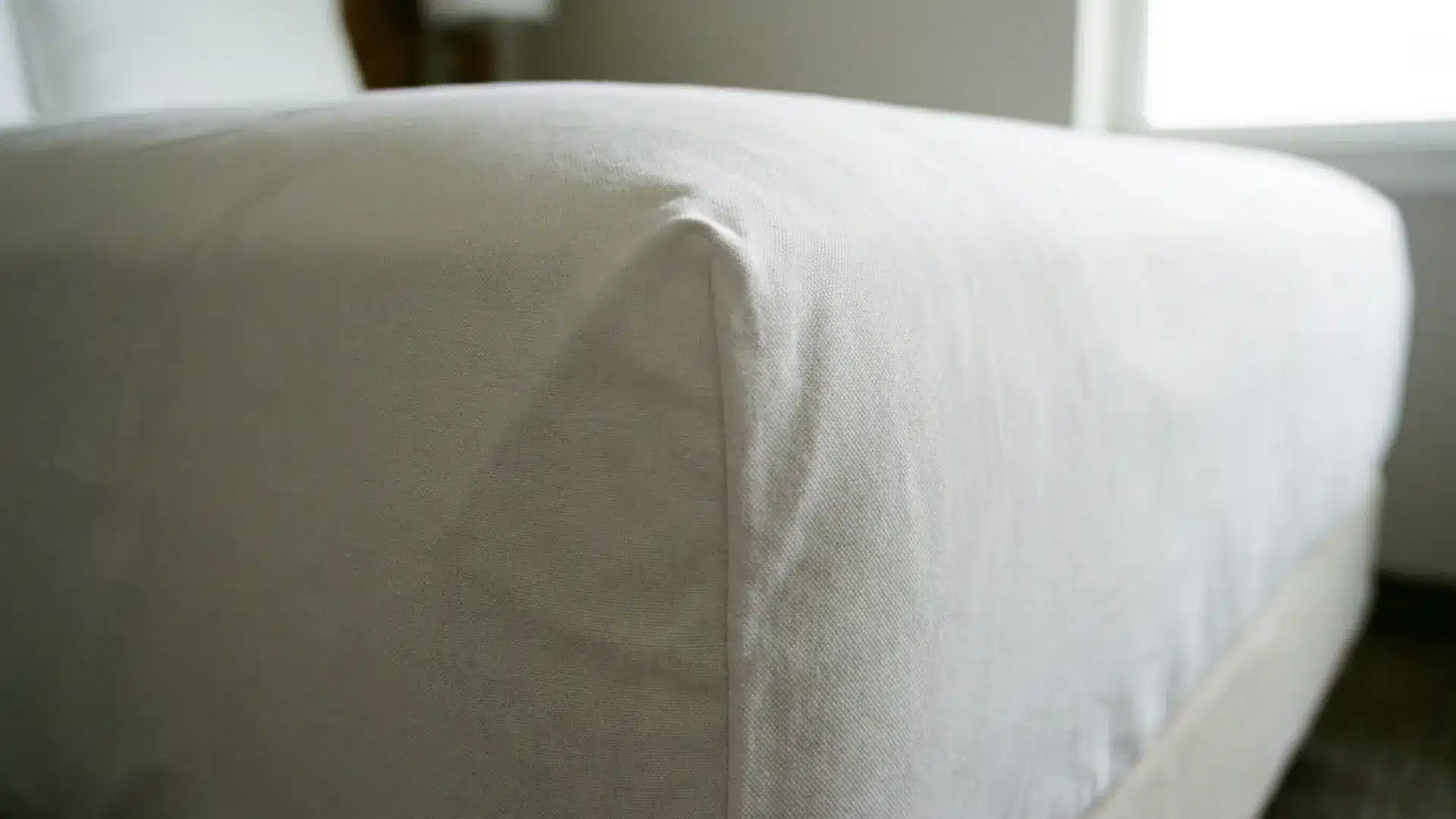 close-up of crisp white percale cotton sheet tucked tightly at guest bed mattress corner