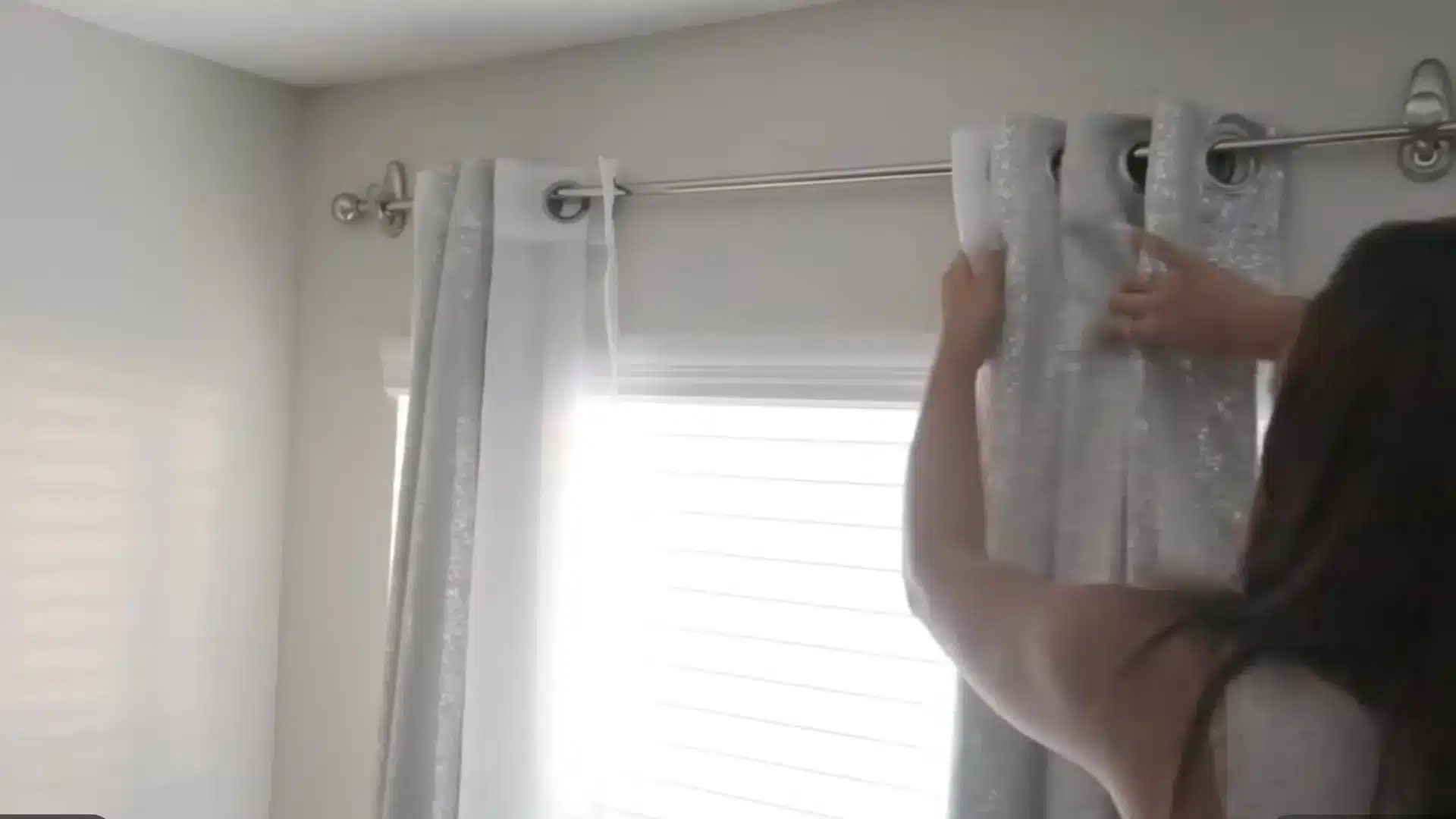 woman sliding grommet curtain panel onto rod mounted with command hooks