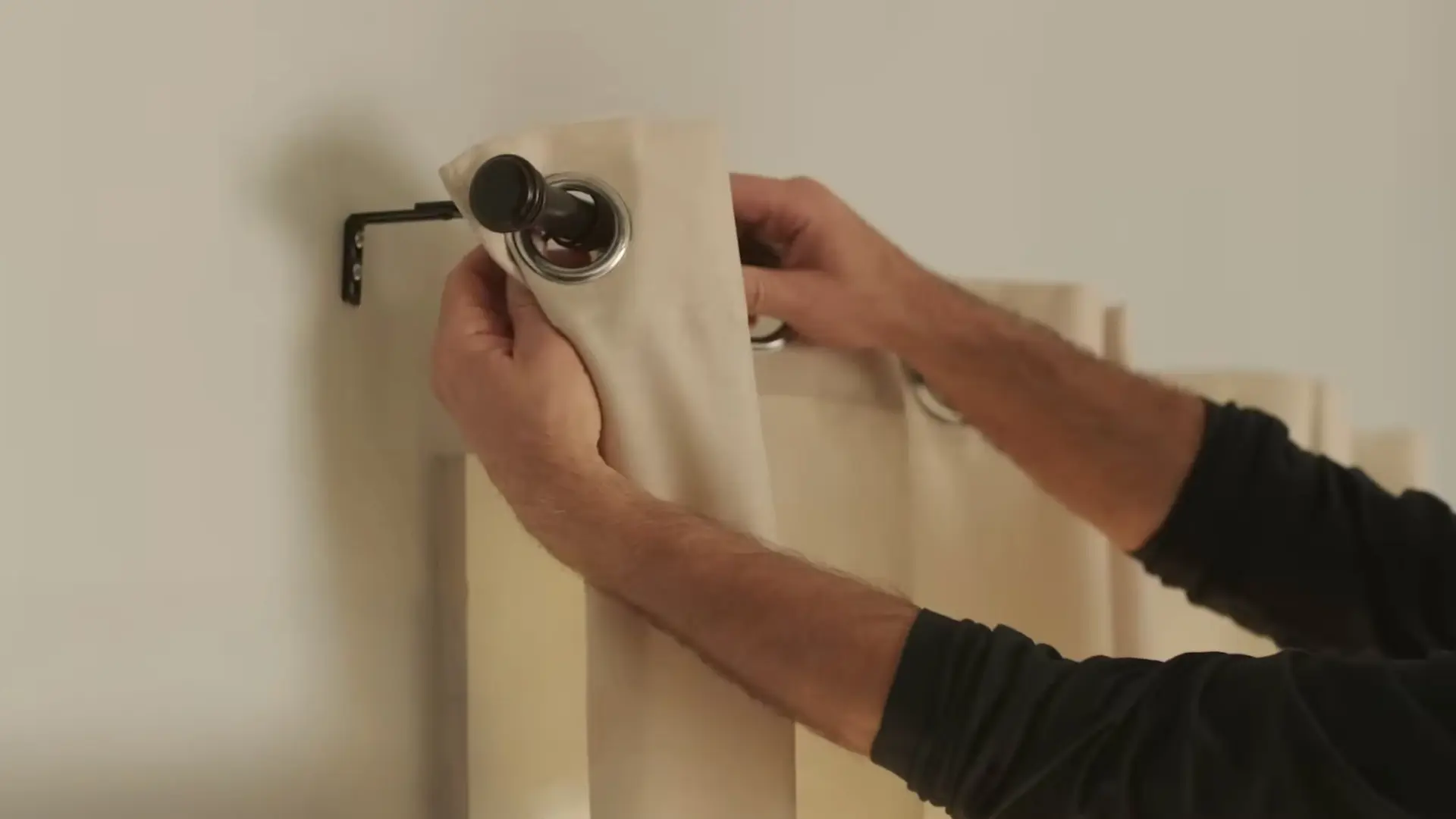hanging cream curtain panel onto rod finial with bracket mounted on wall