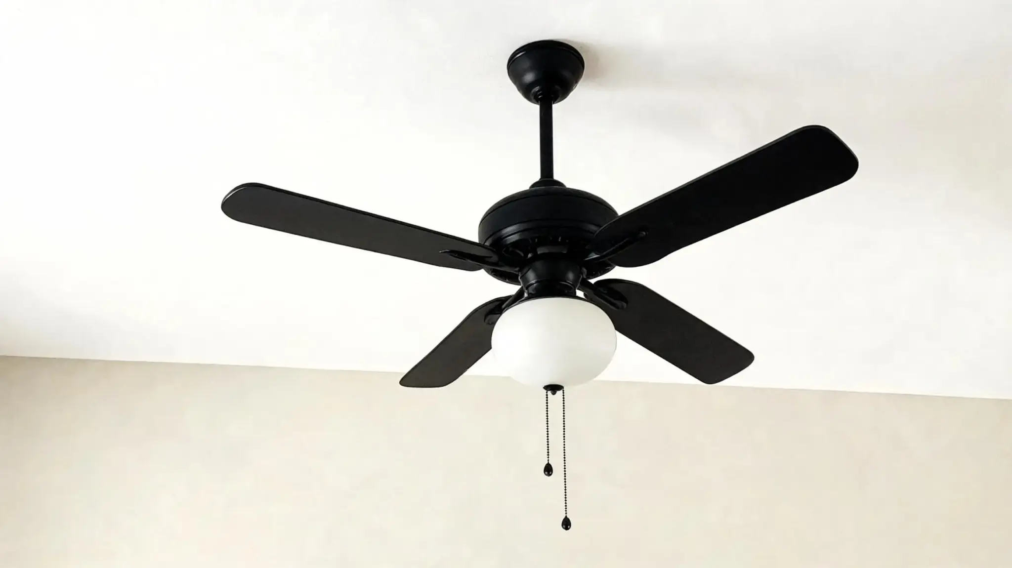 black five-blade ceiling fan with a frosted glass light fixture hangs from a white ceiling