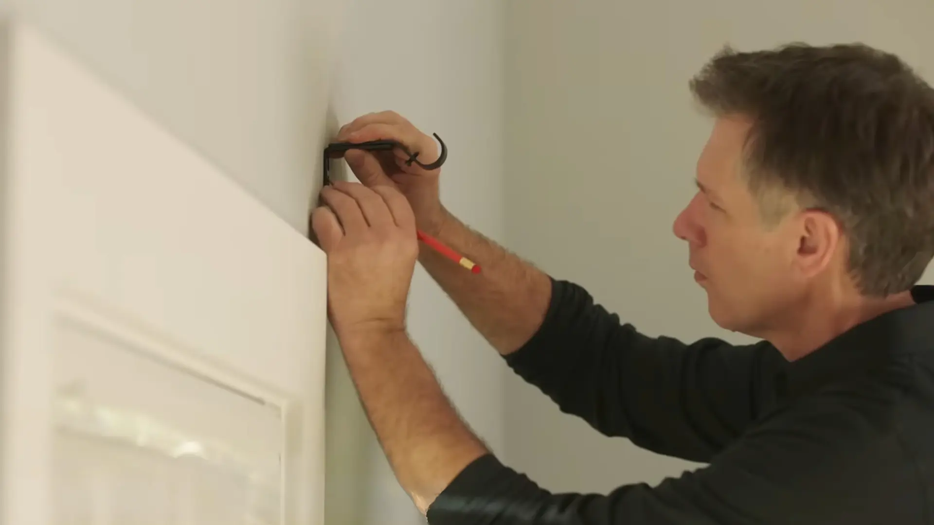 man using allen key to secure curtain rod bracket against drywall before drilling