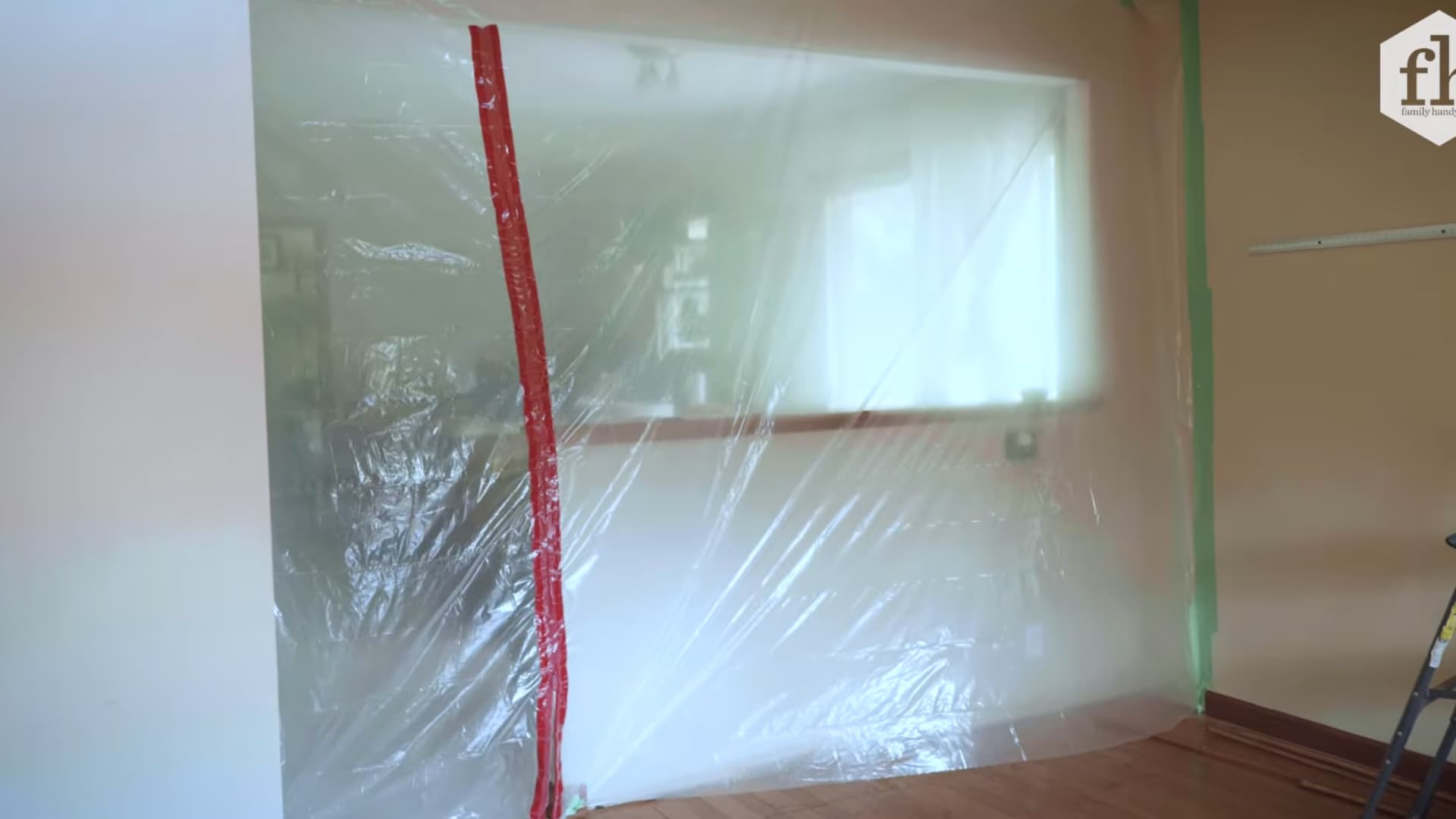 worker prepping hardwood floor room with plastic sheeting and painter's tape