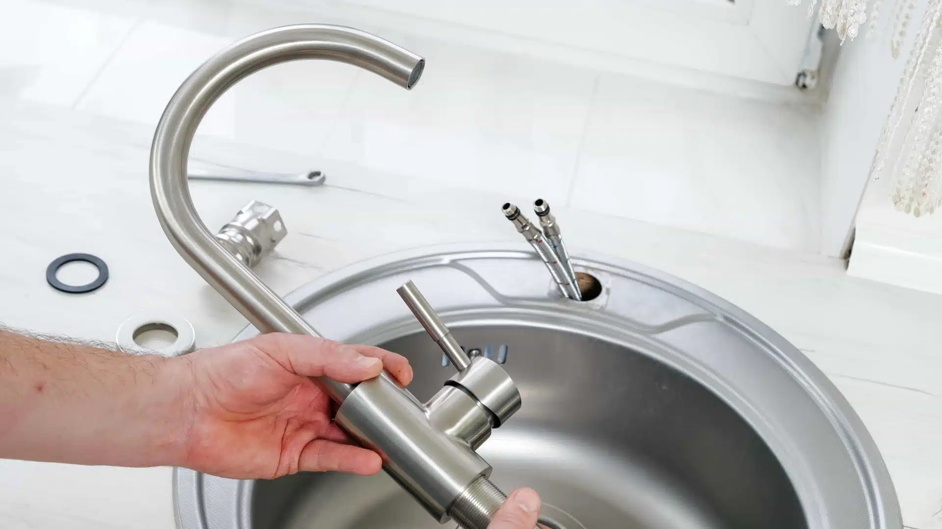 hands assemble a brushed nickel kitchen faucet over a stainless steel sink with connected water lines