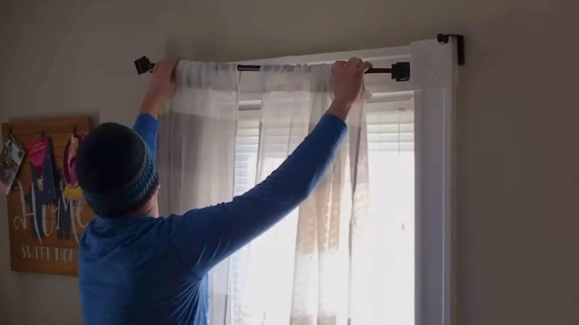 man hanging sheer white curtain on window attachment clips without drilling