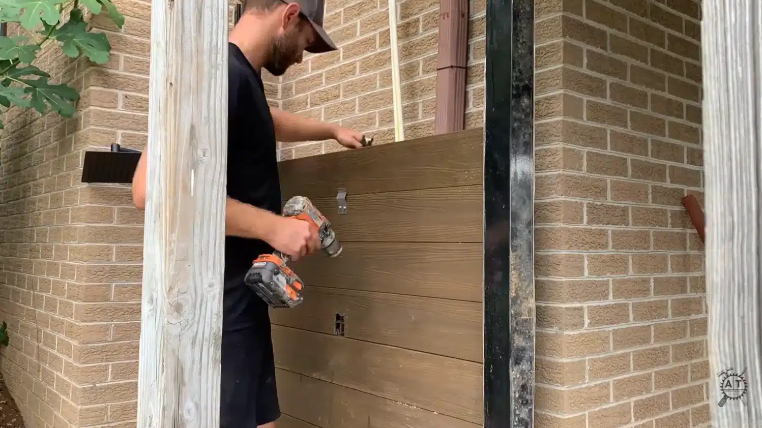 a man drilling composite privacy panel slats into place between two black metal post