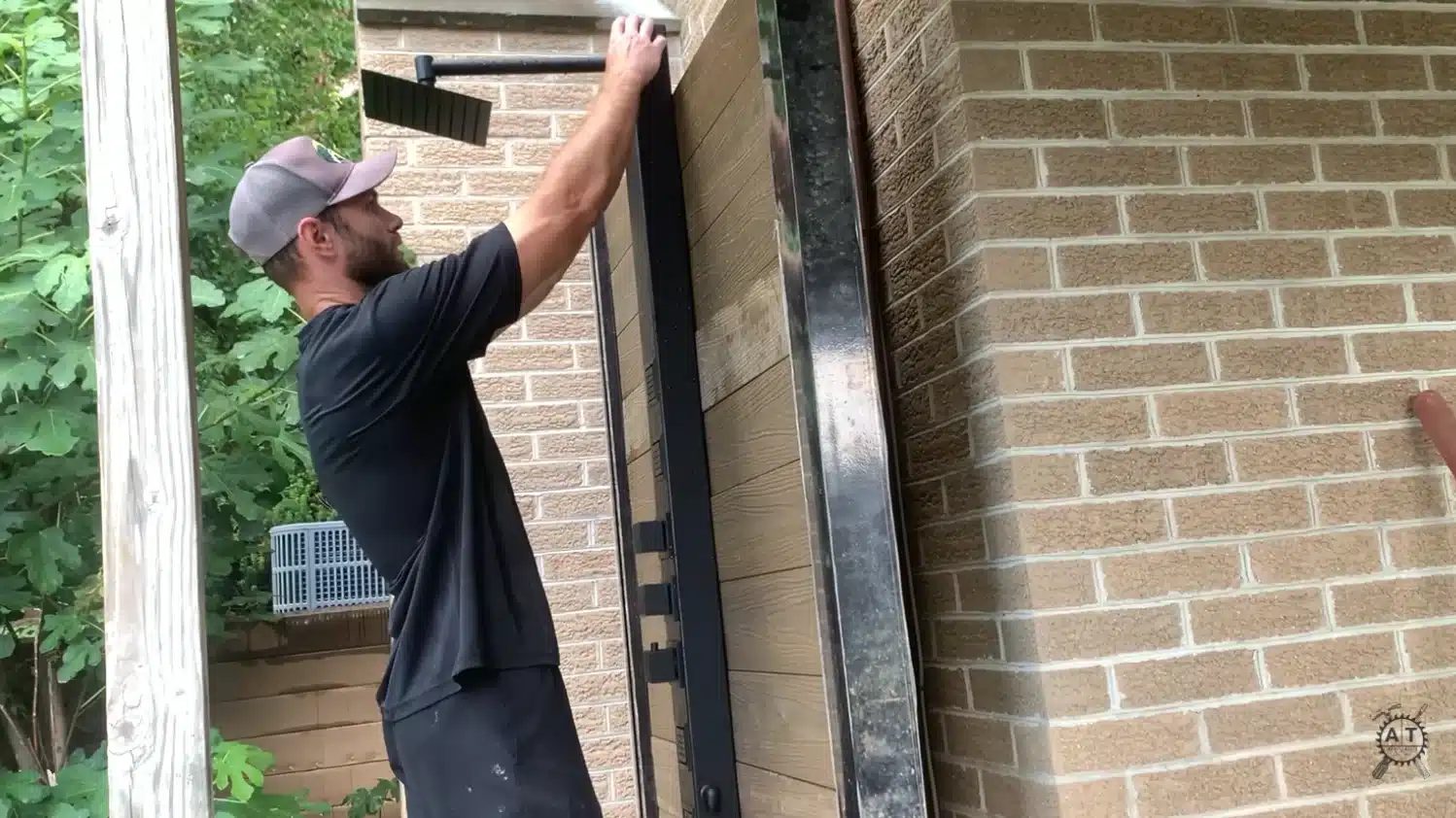 a man lifting a black framed glass shower panel into place against a wooden post