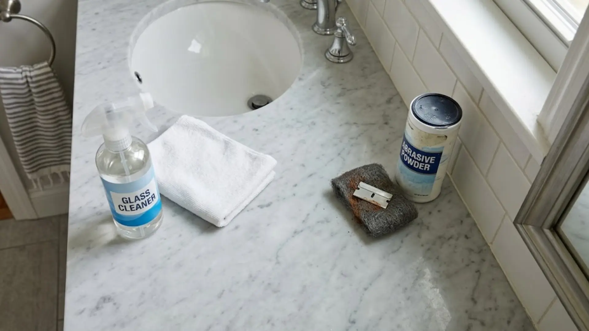 bathroom counter with glass cleaner cloth steel wool razor blade and abrasive powder set aside