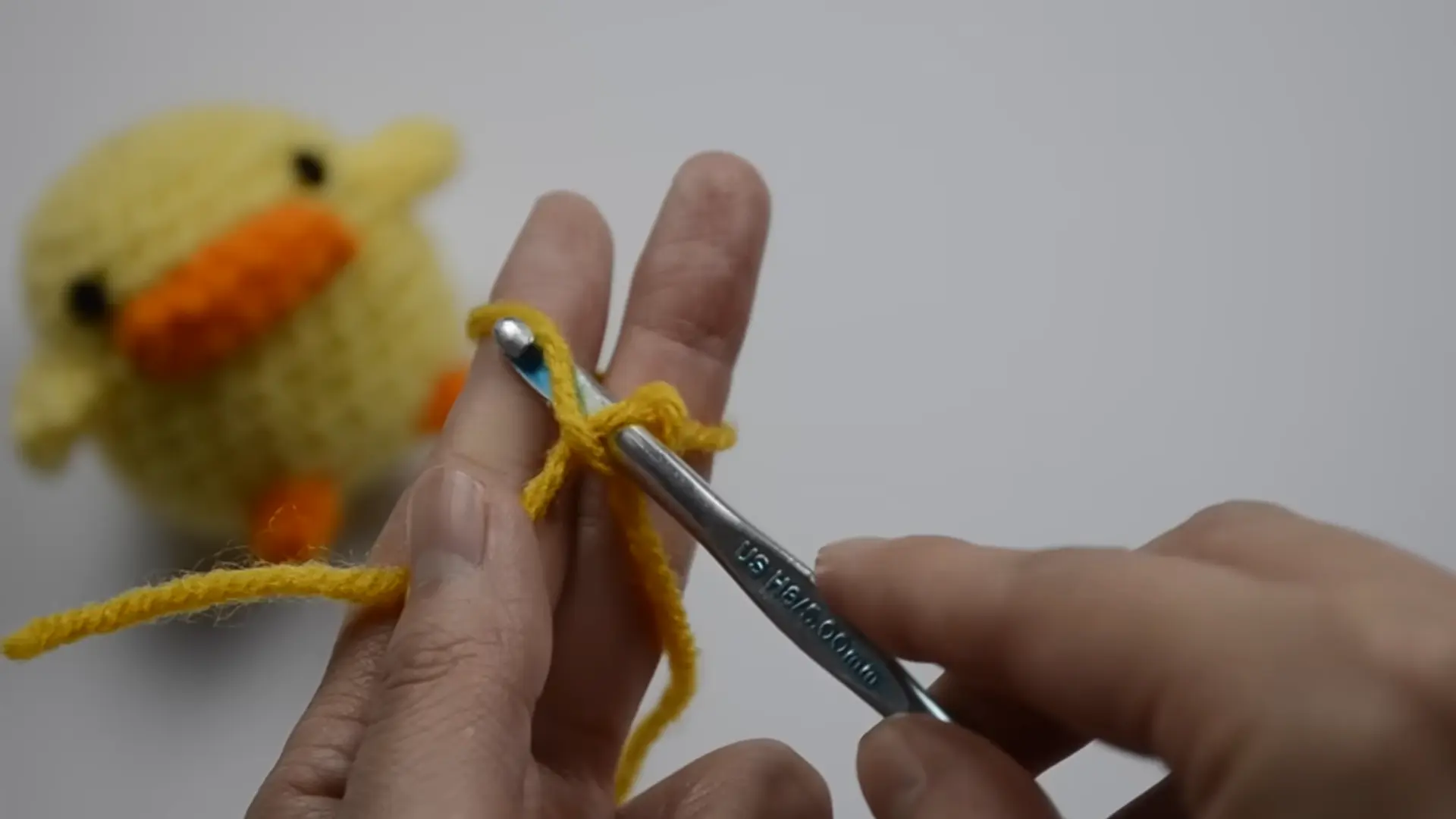 beginner hands creating a crochet slip knot with cream yarn before starting the first stitch