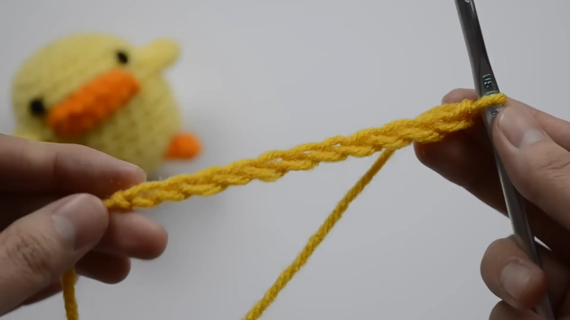 beginner making a long crochet foundation chain with cream yarn and a crochet hook