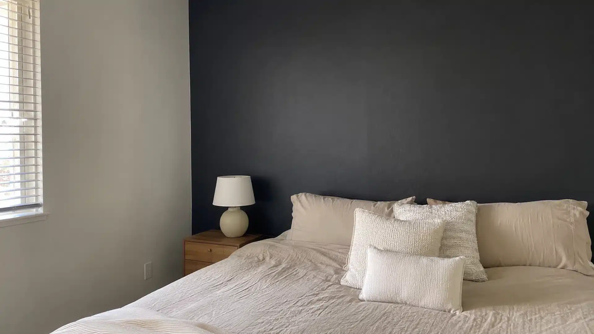 black accent wall behind a bed with cream linen bedding and textured neutral pillows in a warm bedroom
