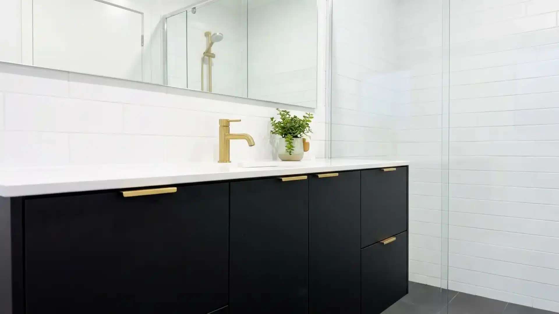 black matte cabinet vanity with white countertop gold faucet and hardware against white tile