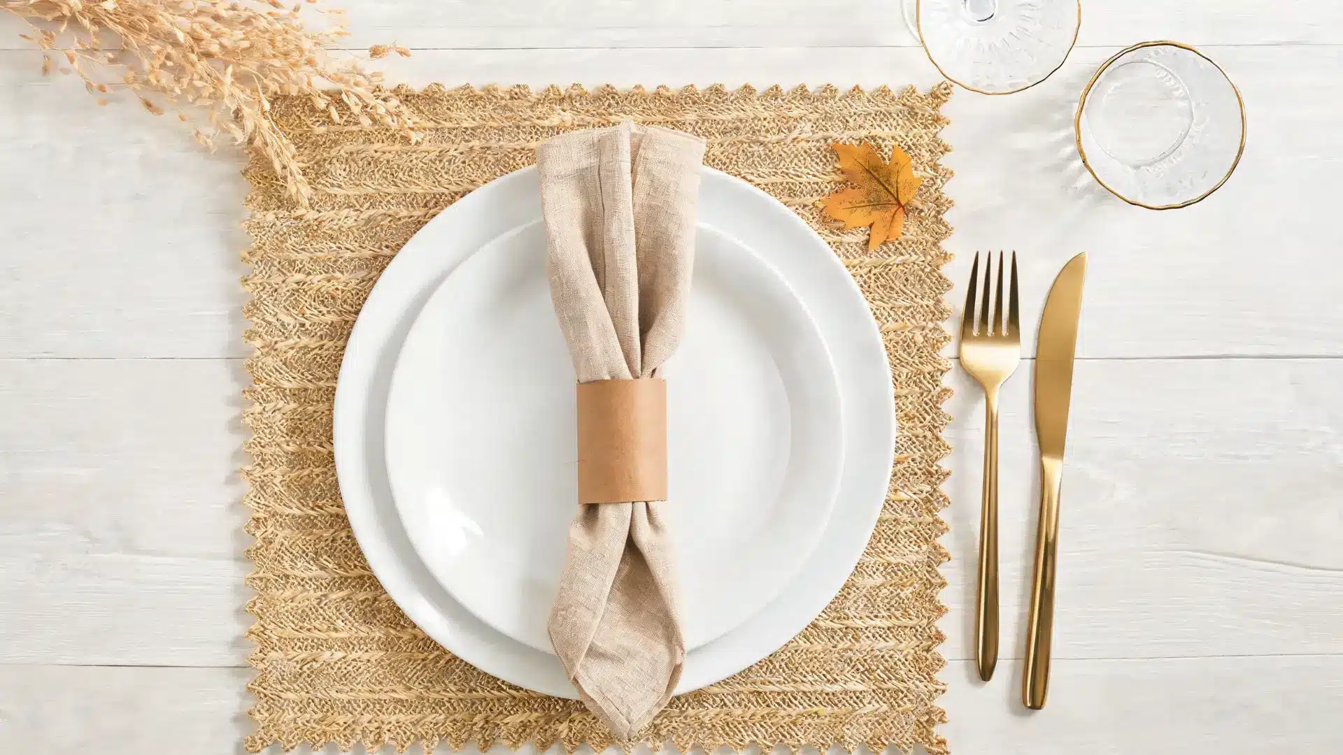 brown paper napkin ring on a linen napkin, white plates, gold flatware, and woven placemat
