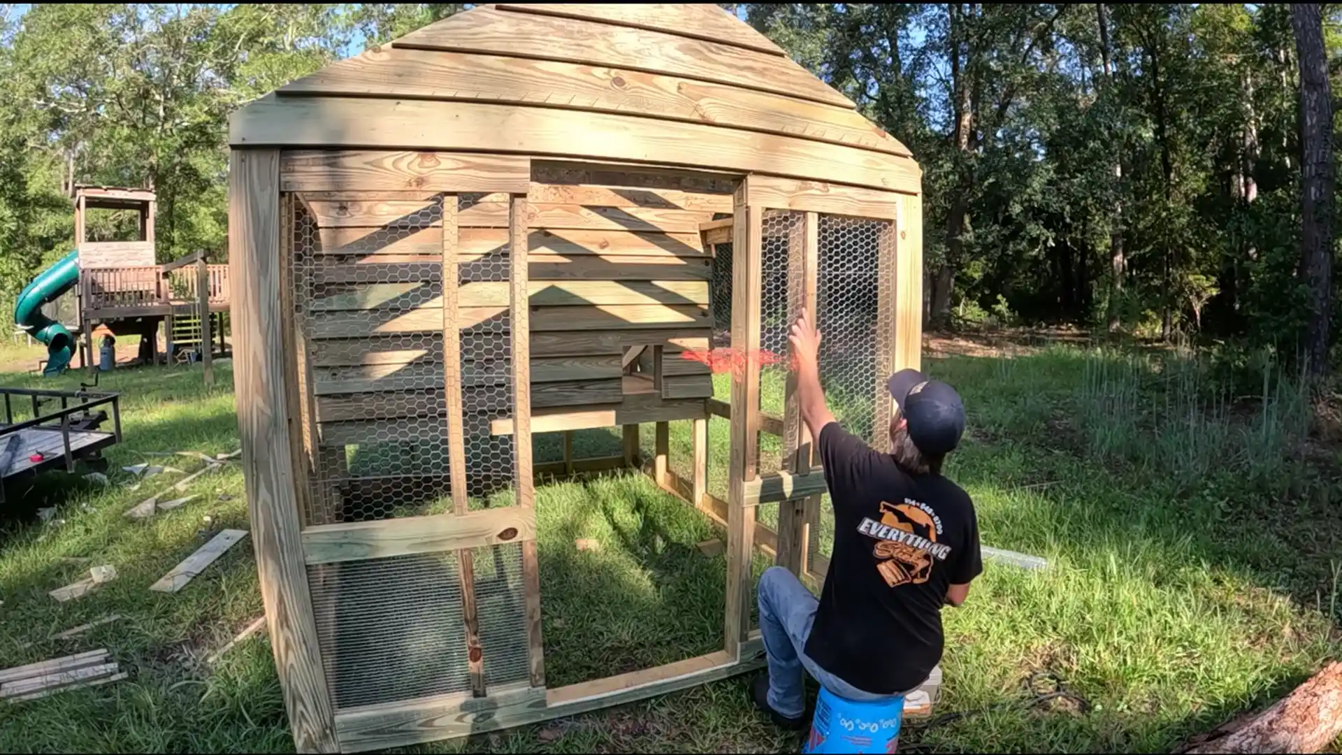 builder installing trim and door on a finished diy chicken coop with slat siding and chicken wire