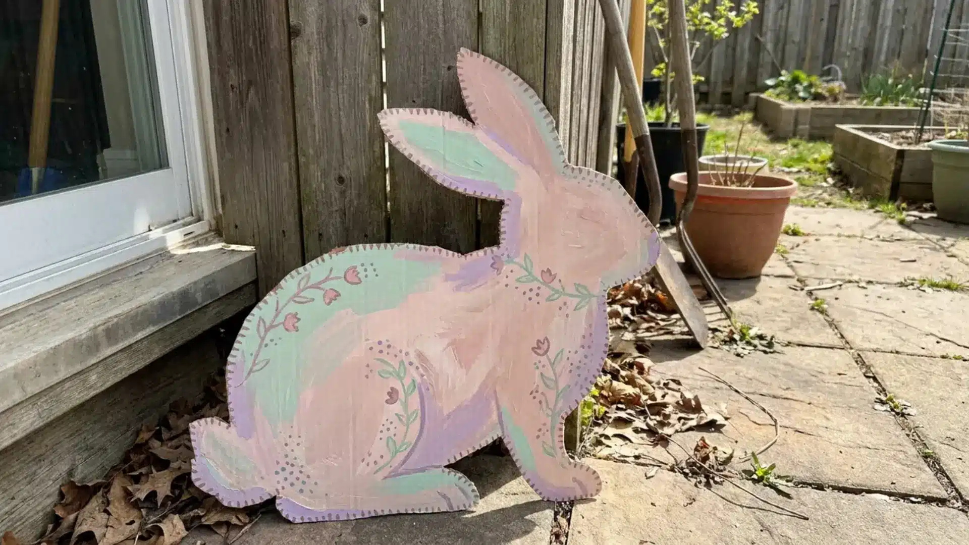 cardboard bunny cutout painted in soft pastel colors with a hand painted floral design outdoors