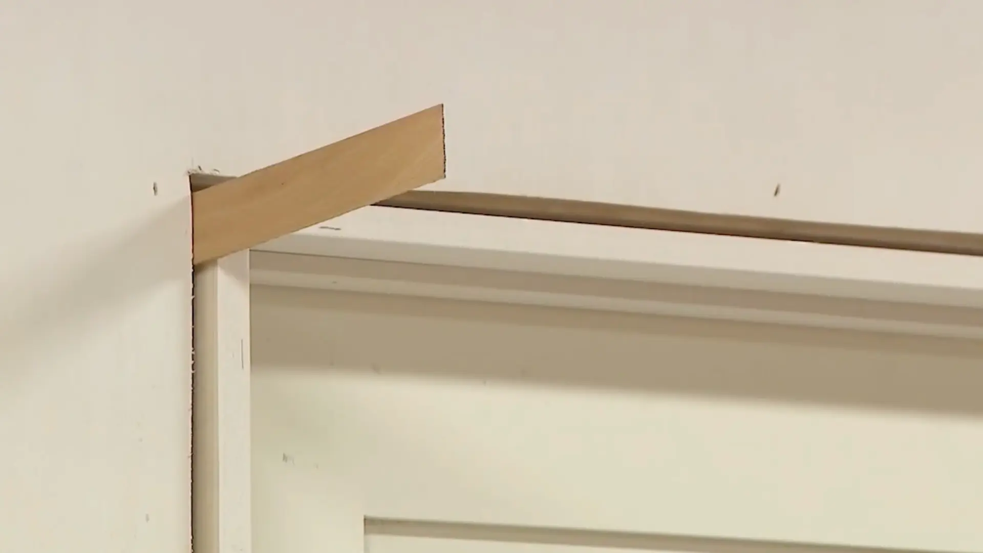 close up of a wood shim wedged into the gap above a door frame jamb
