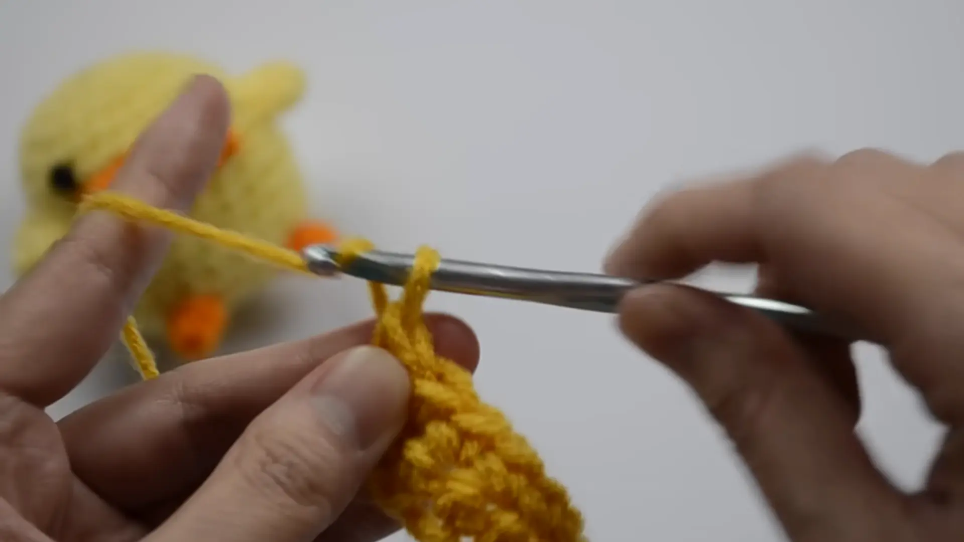 close-up of beginner completing a single crochet stitch with cream yarn and a crochet hook