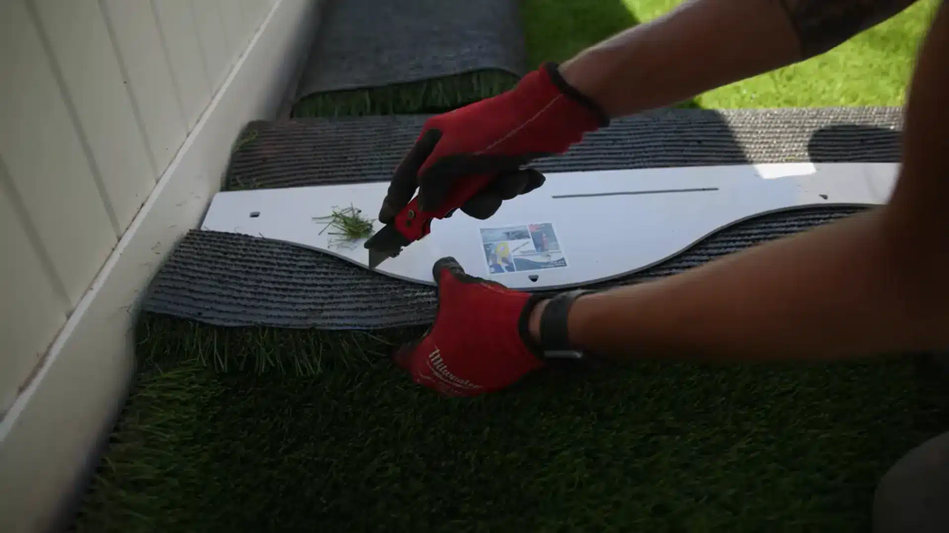 close-up of hands trimming artificial grass backing with a utility knife for a precise edge fit