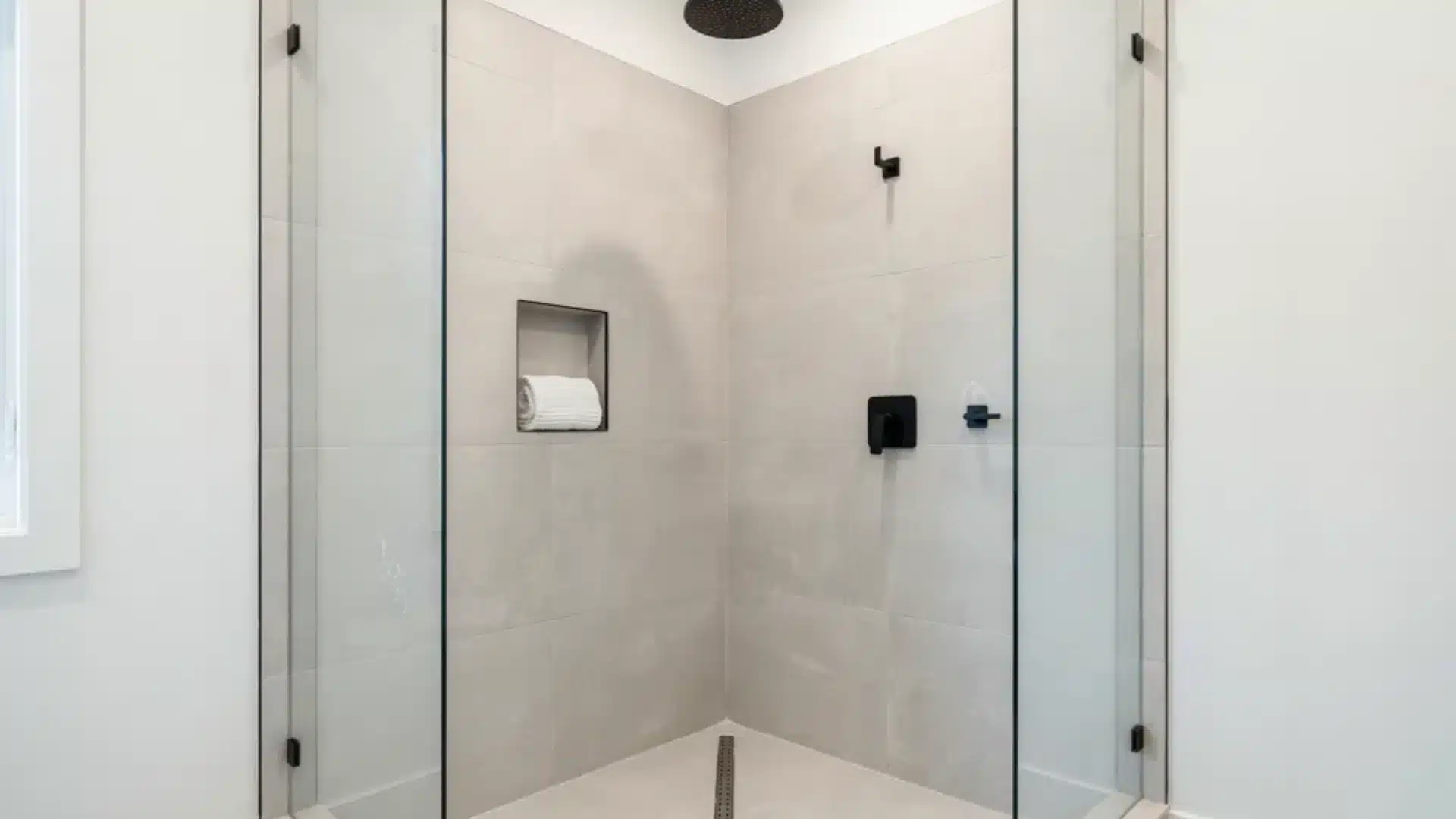 corner curbless shower with two glass panels gray tile and black fixtures throughout
