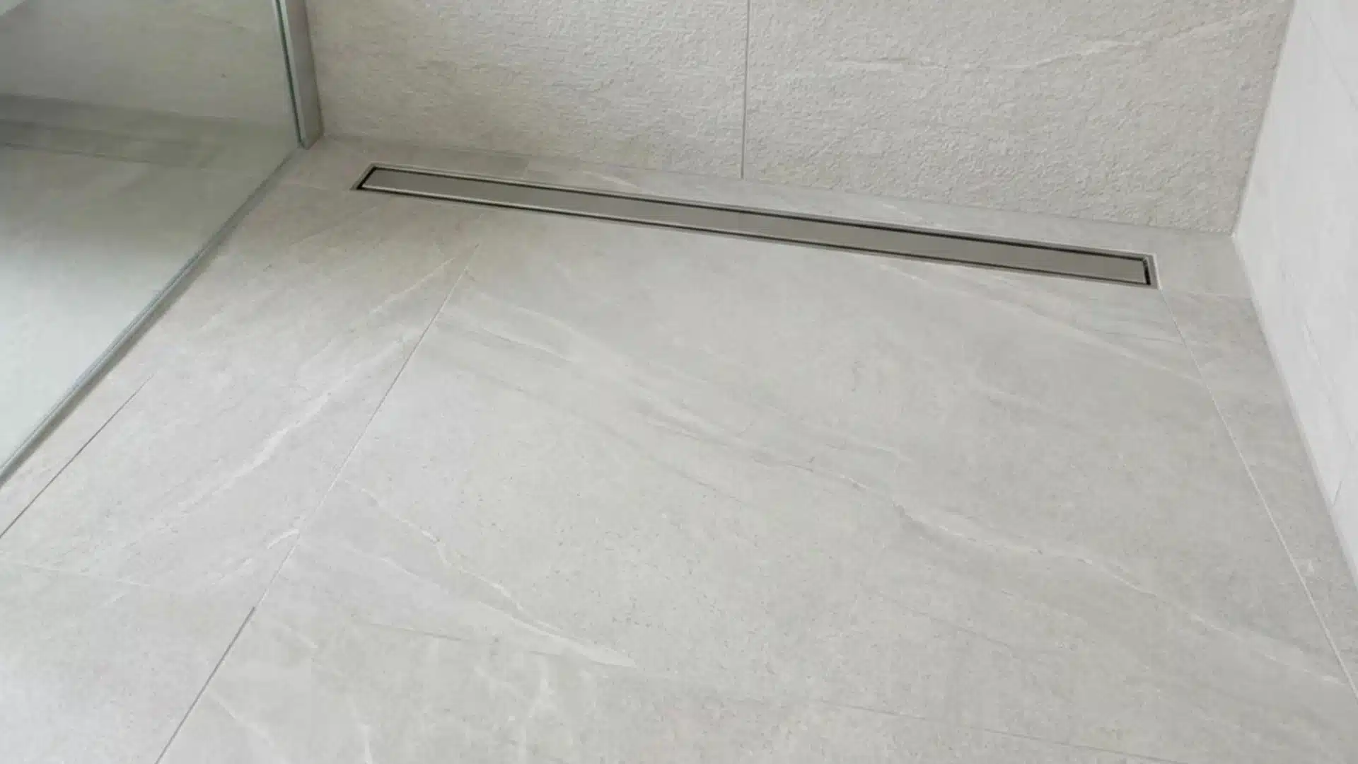 curbless shower closeup with linear stainless drain and light travertine look tile floor