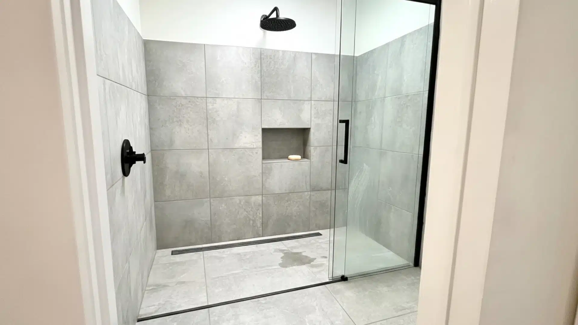 curbless shower doorway view with gray tile black fixtures niche and sliding glass door