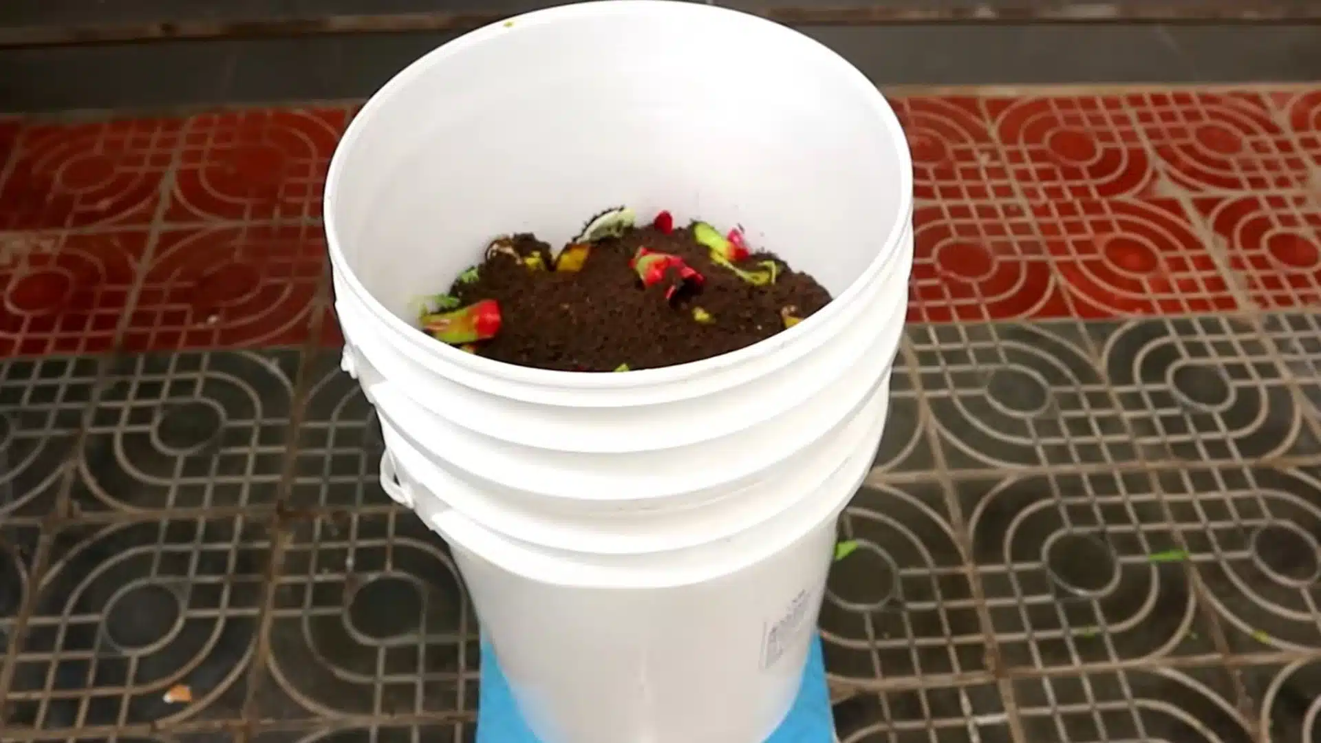 dark compost mixture layered with kitchen scraps inside a white bucket