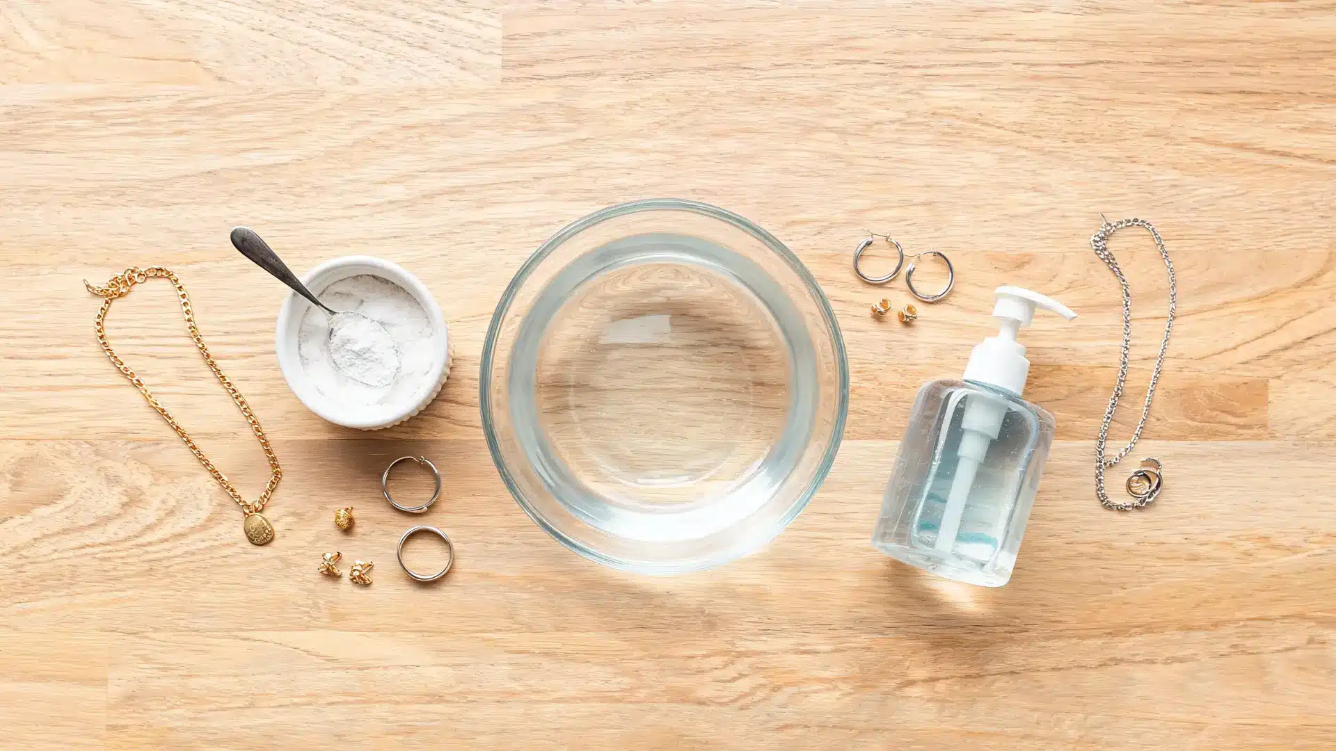 diy jewelry cleaner setup with water, soap, baking soda, necklaces, rings, and earrings on a table