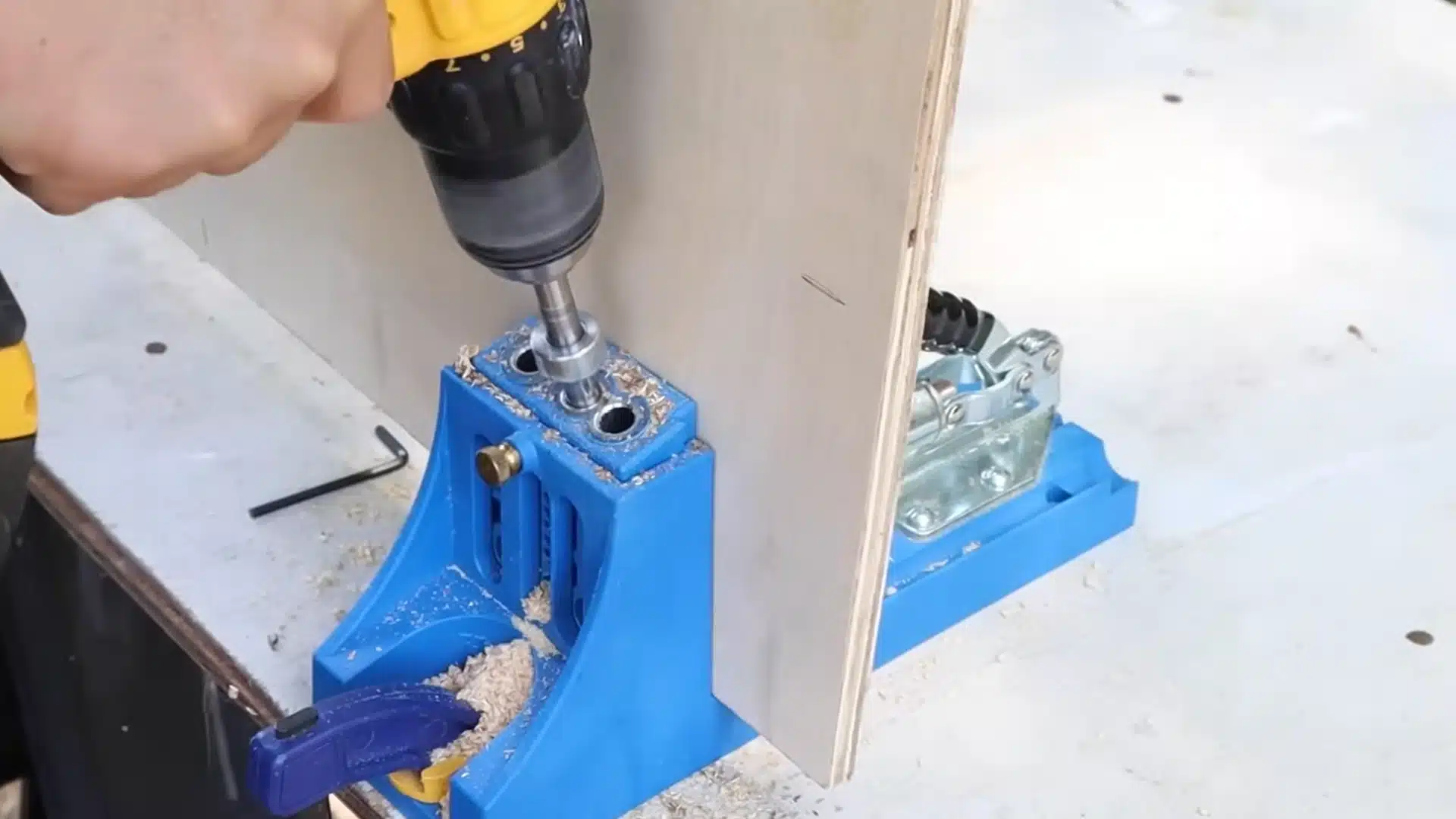 drilling pocket holes into plywood board using a blue pocket hole jig clamped to a workbench