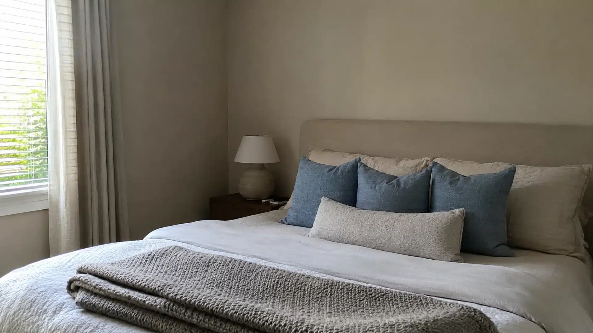 dusty blue throw pillows layered on a taupe bed with a chunky knit blanket in a neutral bedroom