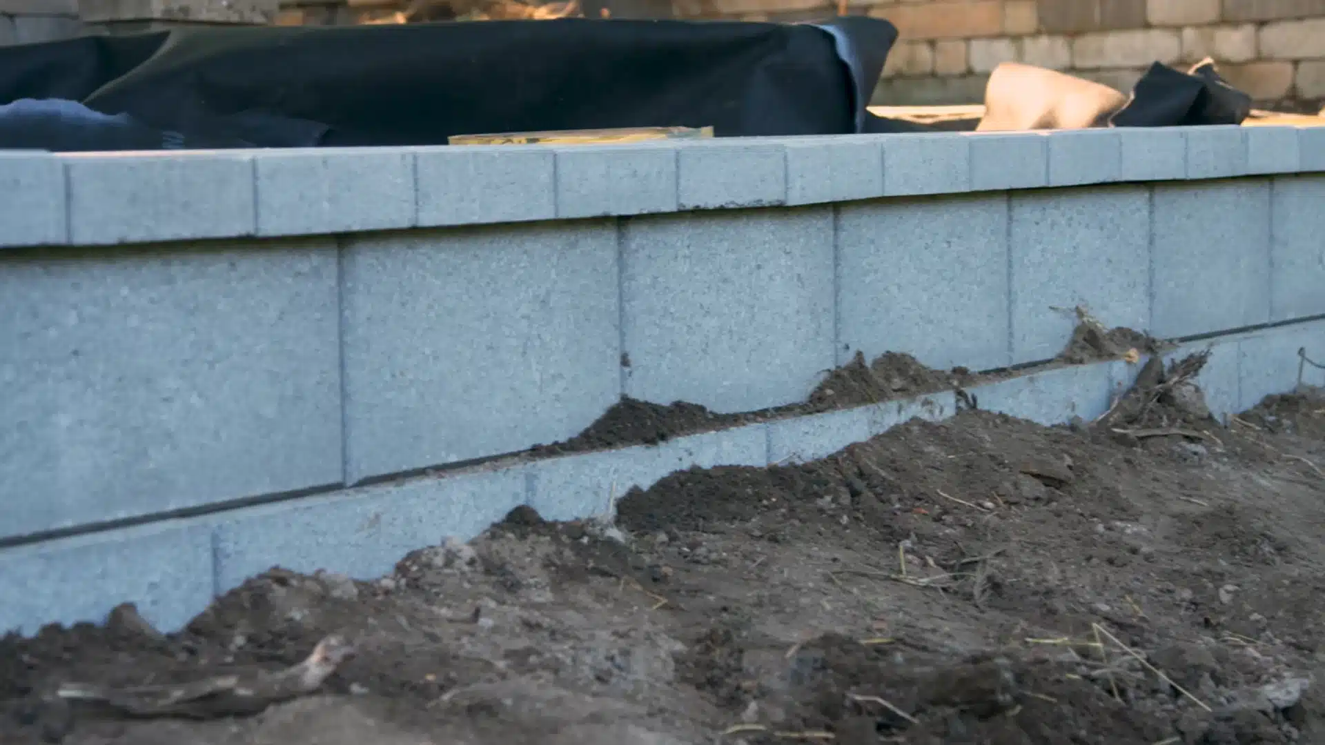 finished segmental block retaining wall top with dirt backfill and landscape fabric visible