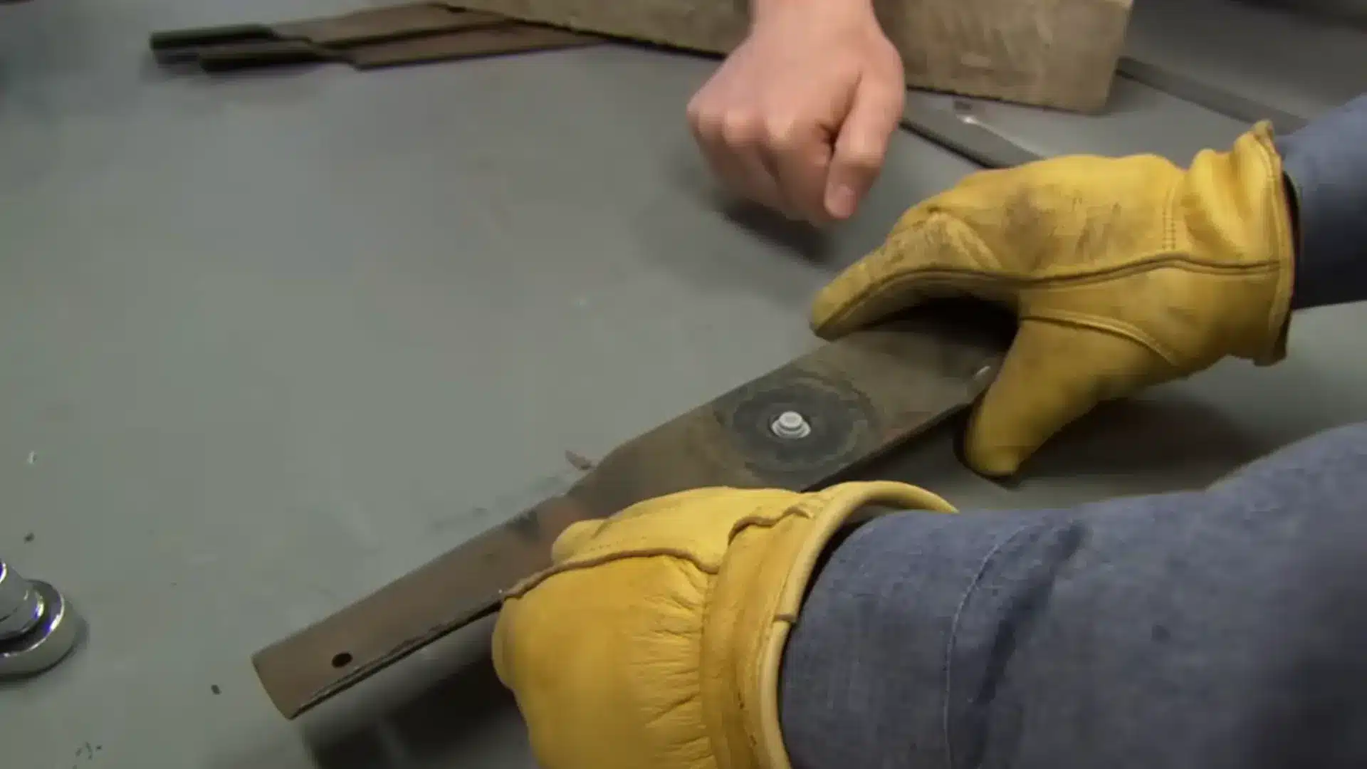 gloved hands checking a sharpened mower blade's balance on the bolt