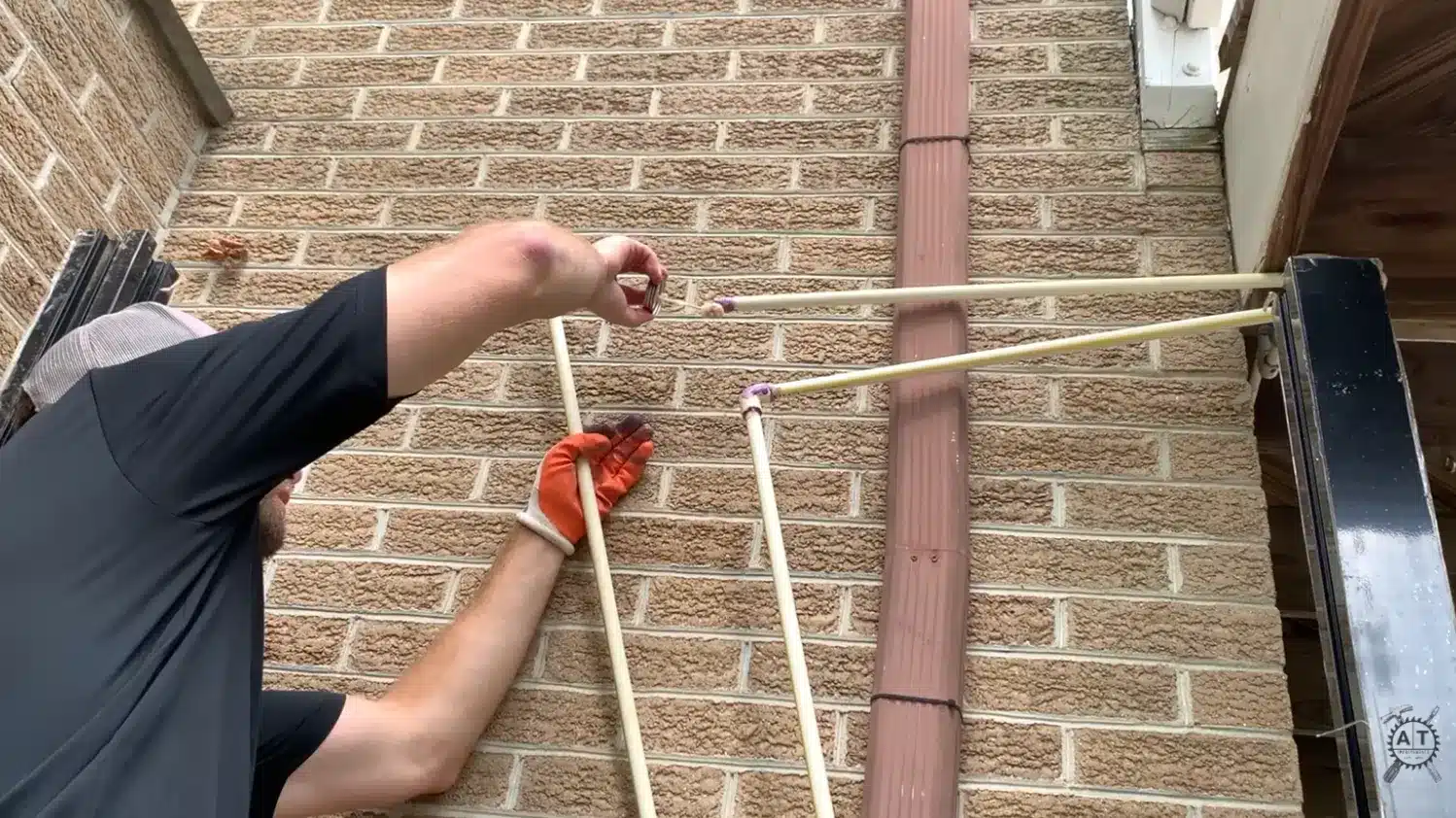 gloved hands gluing cpvc supply pipes together against a brick exterior house wall