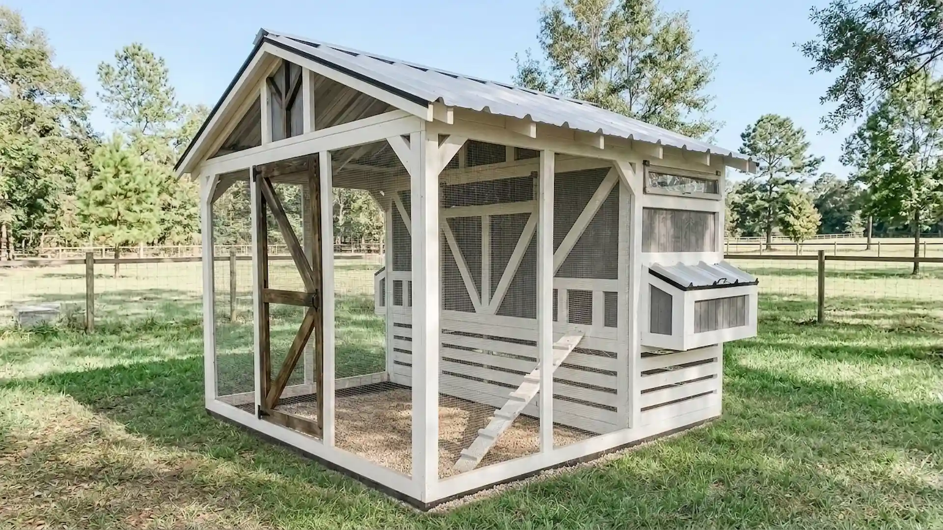 gray and white farmhouse style chicken coop with an open wire run in an open grassy field near a fence