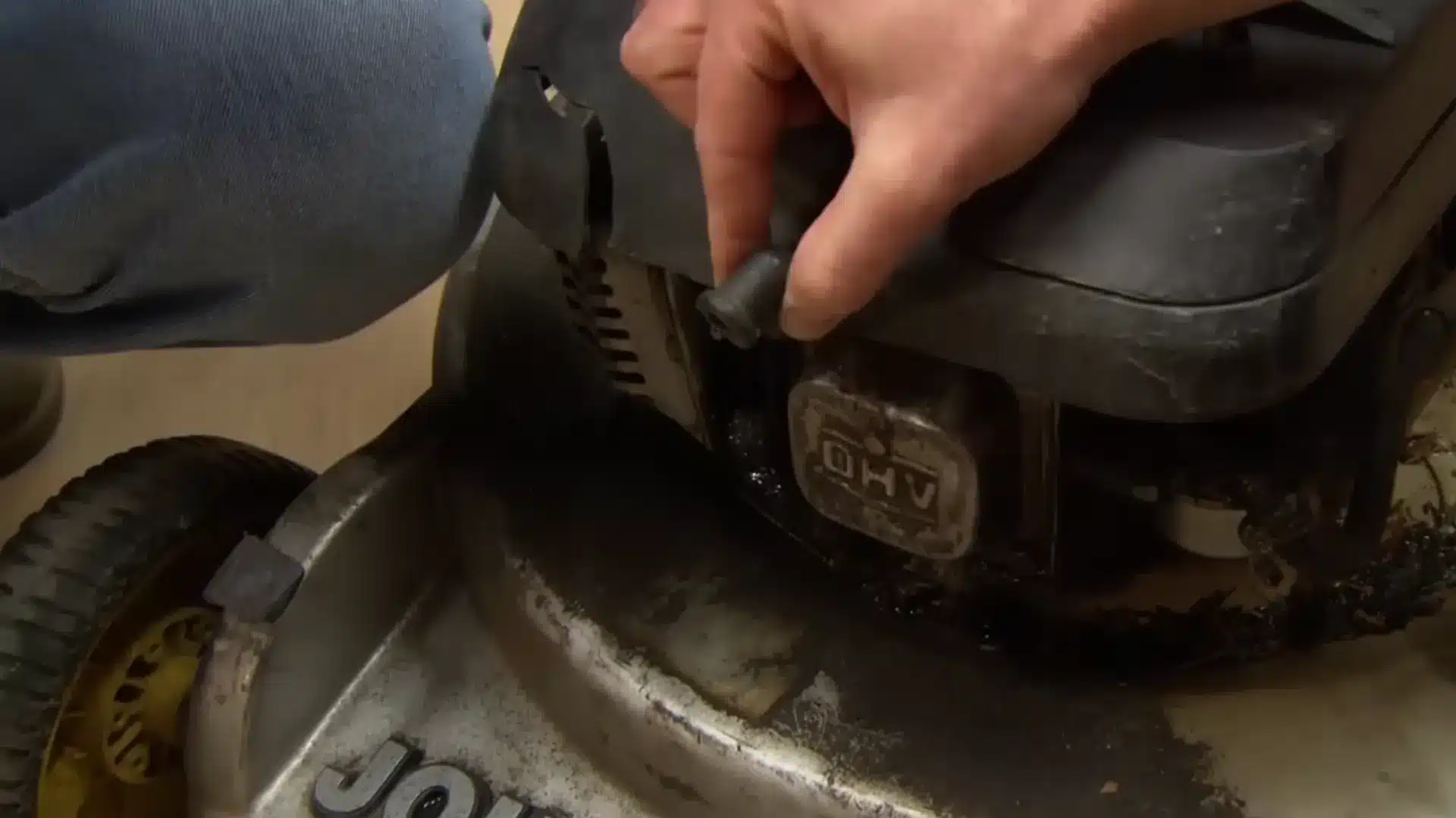 hand disconnecting the spark plug wire on a gas lawn mower engine before maintenance
