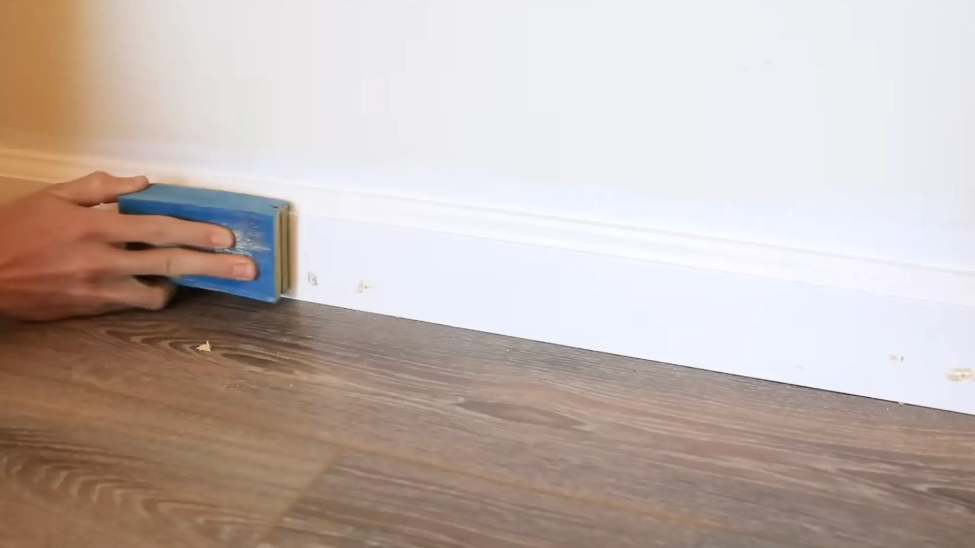 hand sanding filled nail holes on freshly installed white baseboard trim