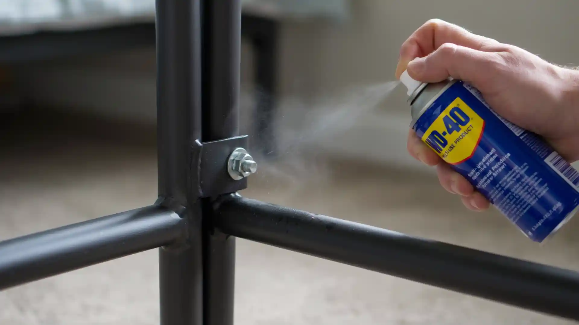 hand spraying lubricant onto a metal bed frame joint to stop squeaking