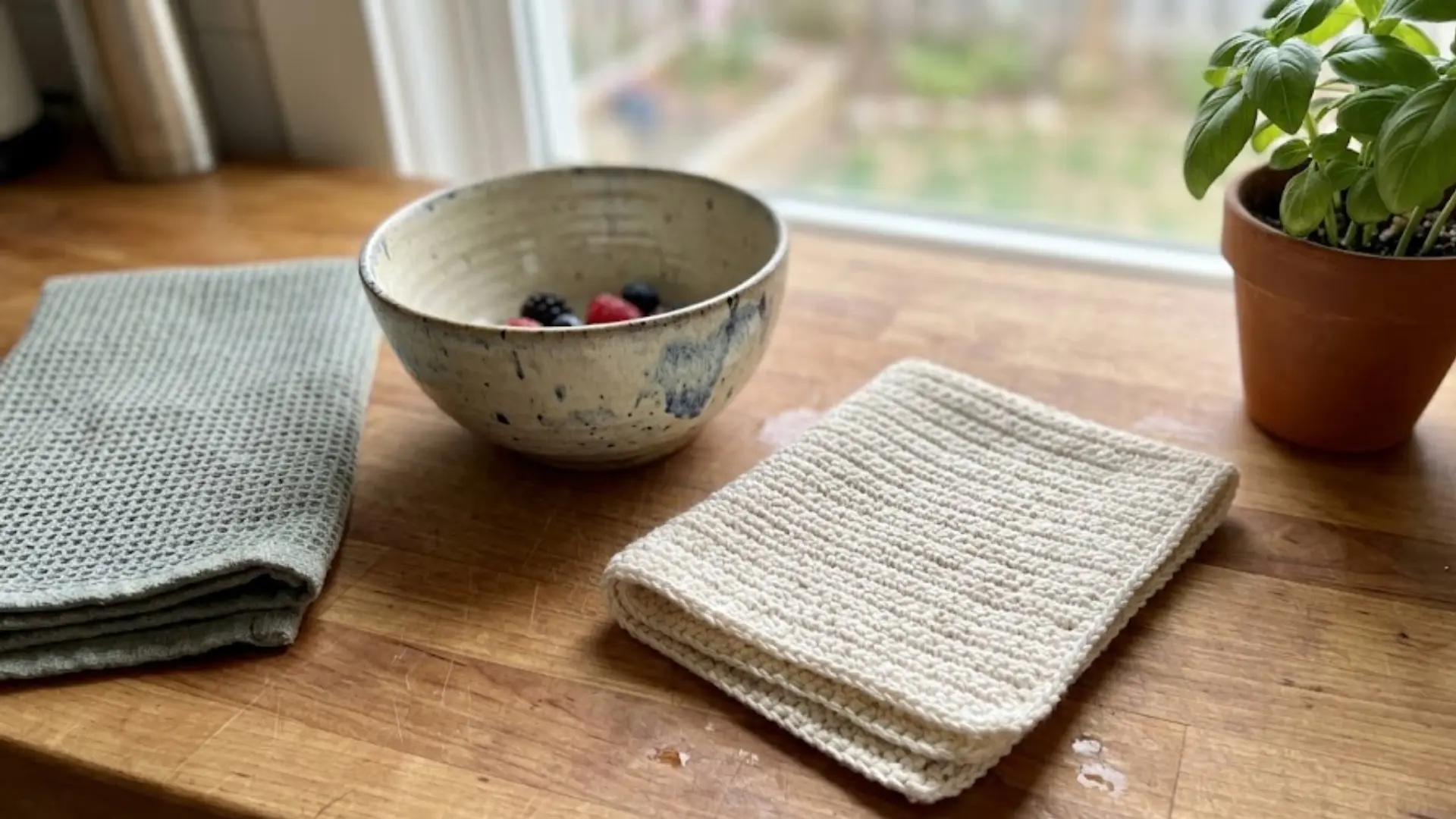 handmade crochet dishcloth folded neatly on a kitchen countertop beside a towel and bowl