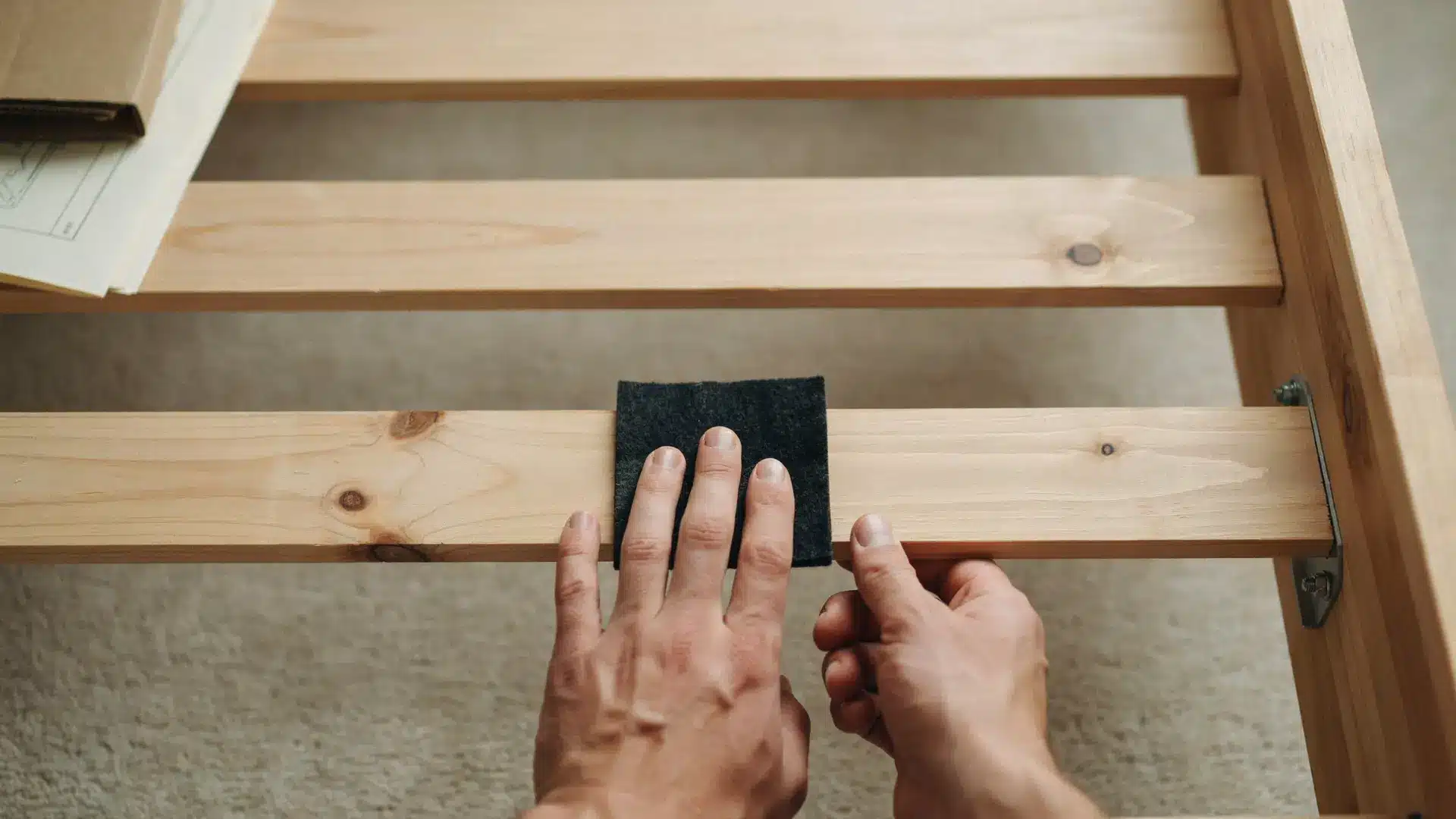 hands placing a felt pad between a bed slat and frame rail
