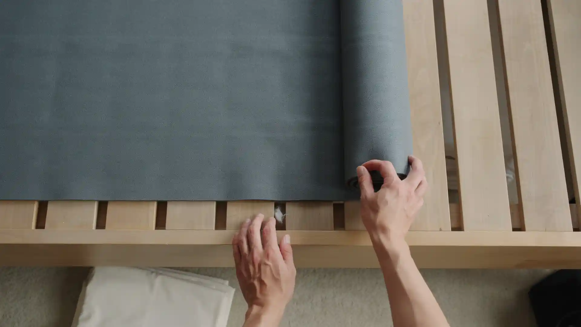 hands placing non-slip mat over wooden bed slats to reduce noise