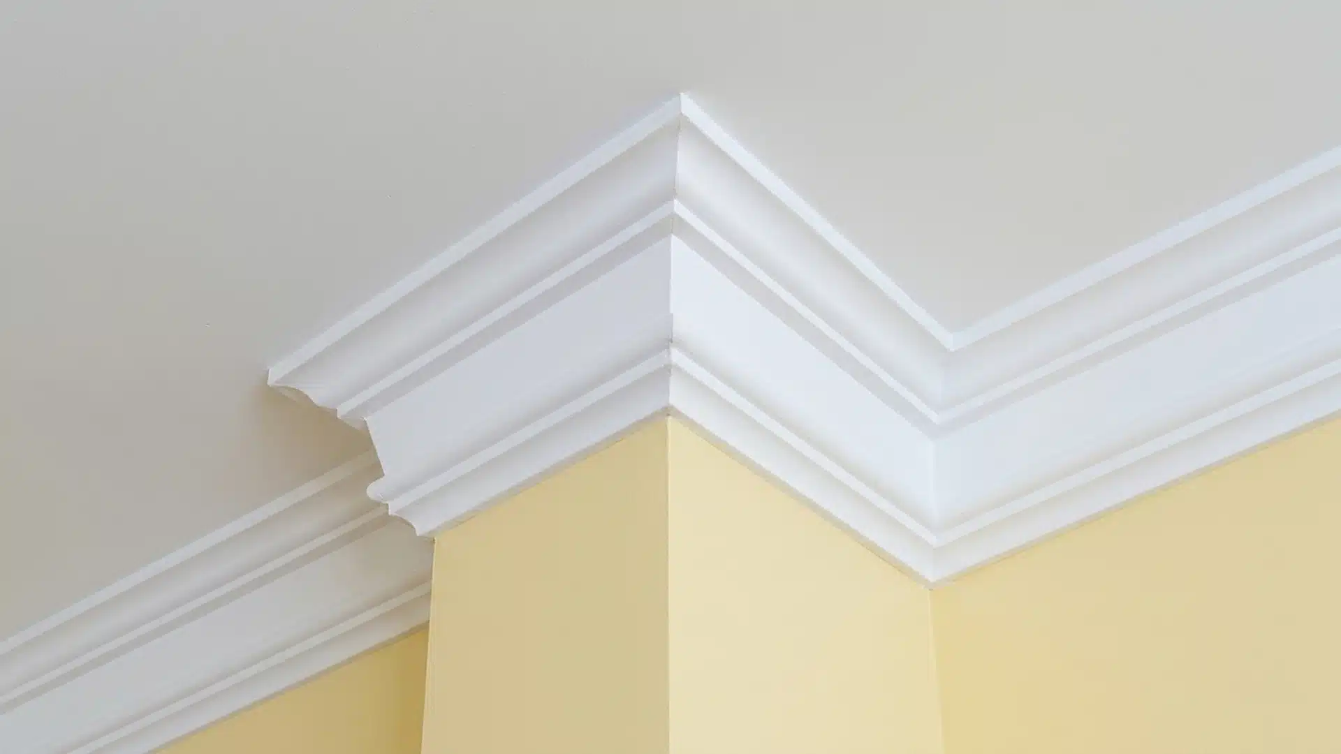 close up of white multi tier crown molding meeting at an outside corner above pale yellow room walls