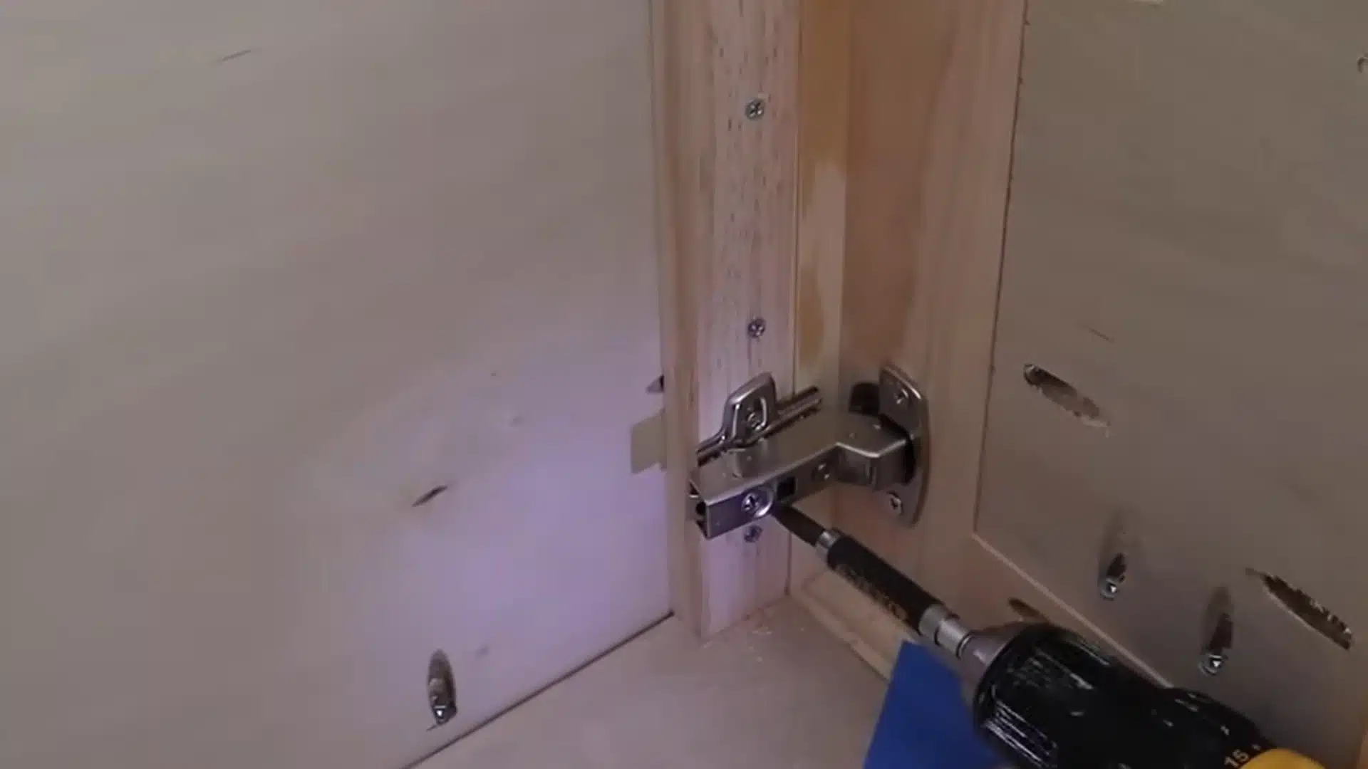 installing a concealed european hinge into a cabinet door frame using a drill and screws