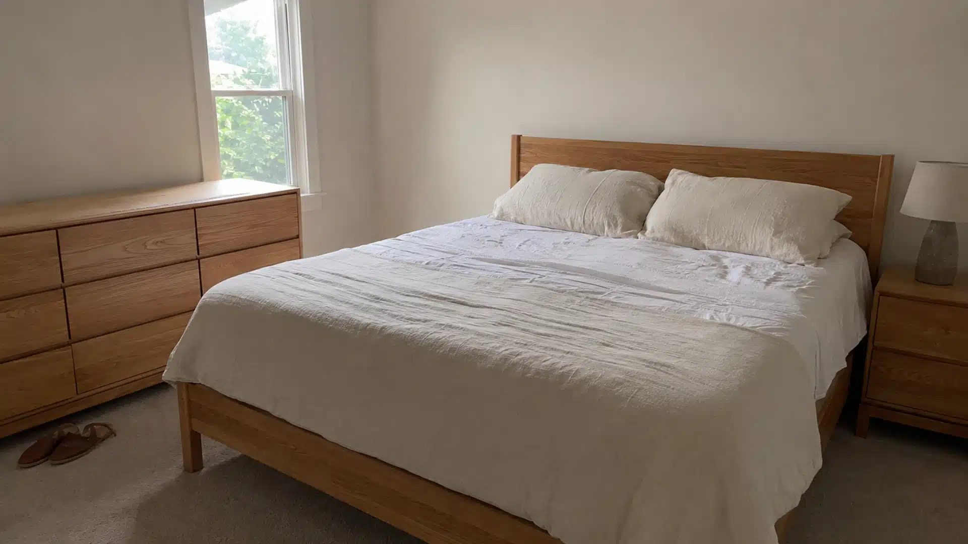 light oak bed and dresser with warm white walls and linen bedding