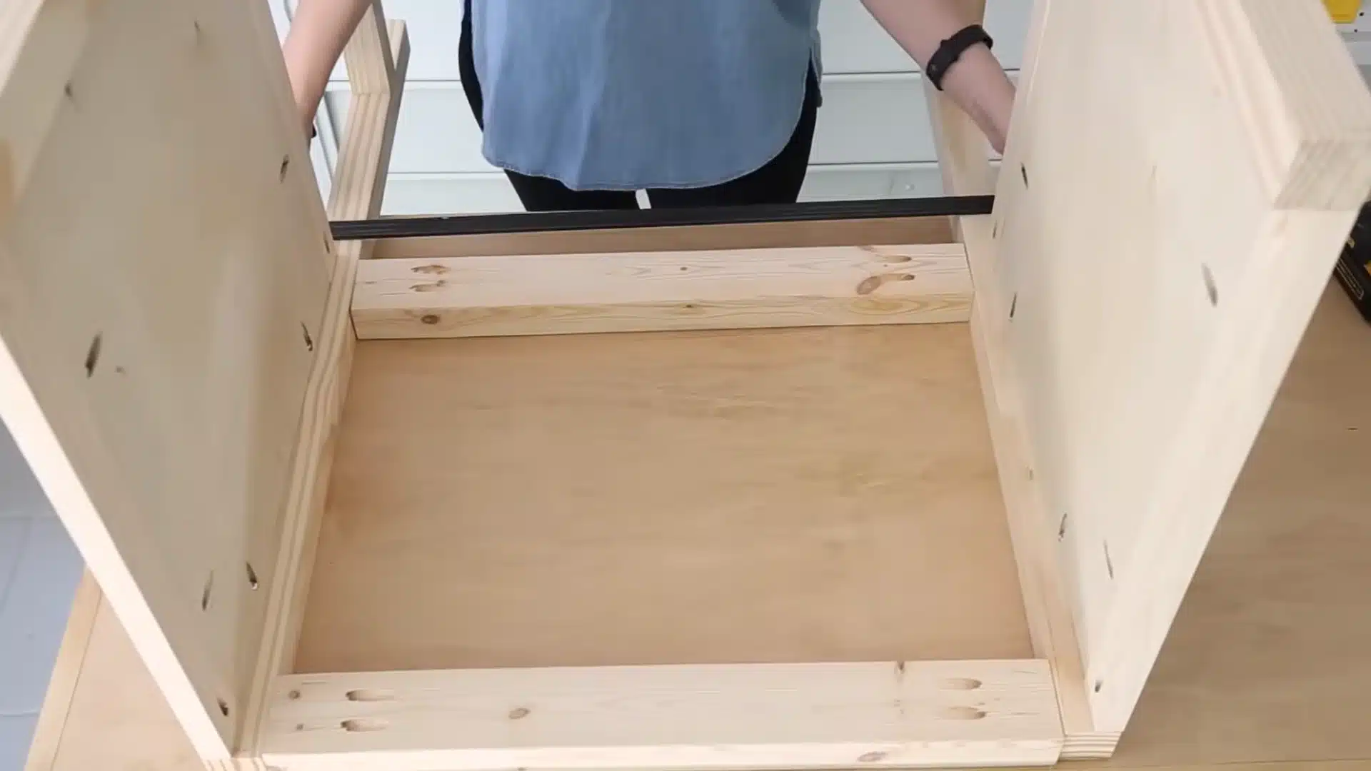 looking inside an open vanity cabinet frame showing the back support boards and open plumbing space