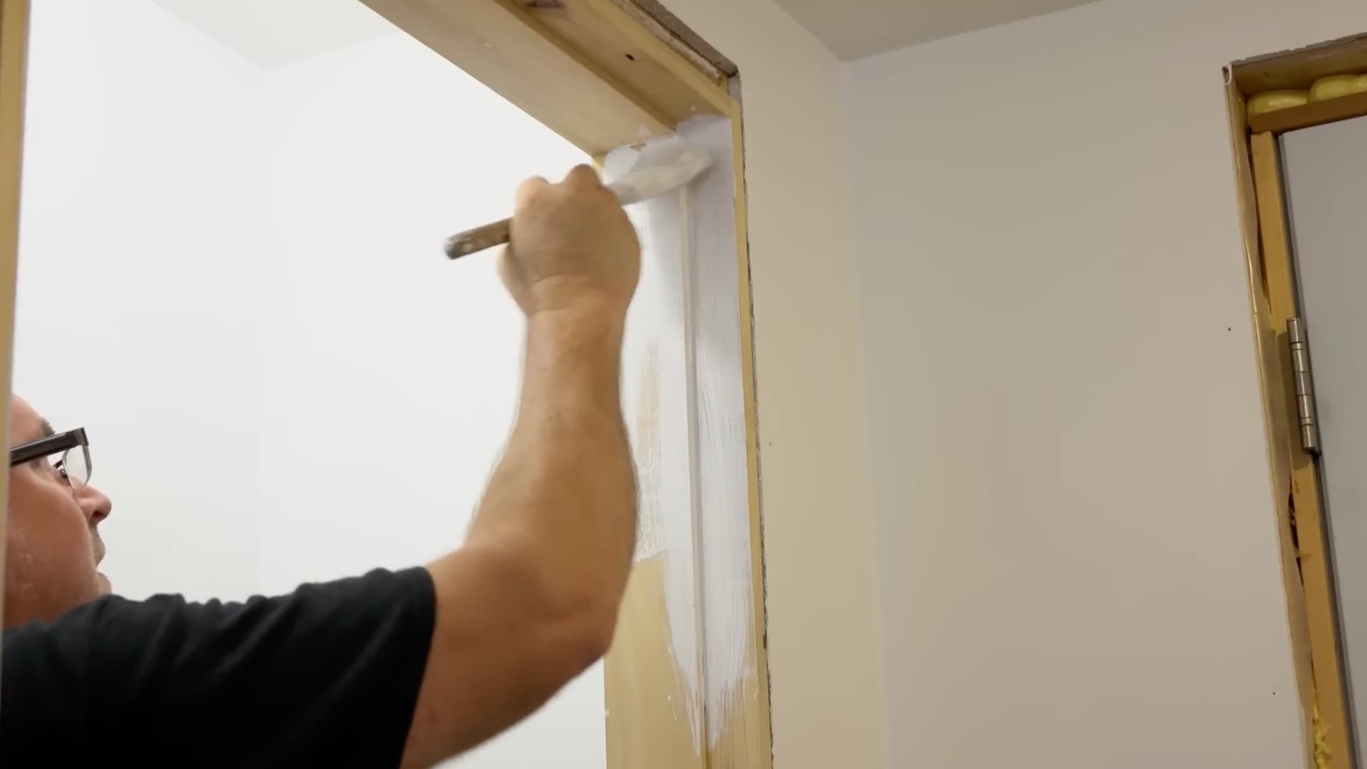 man applying primer with paintbrush along the edge of a finished door frame