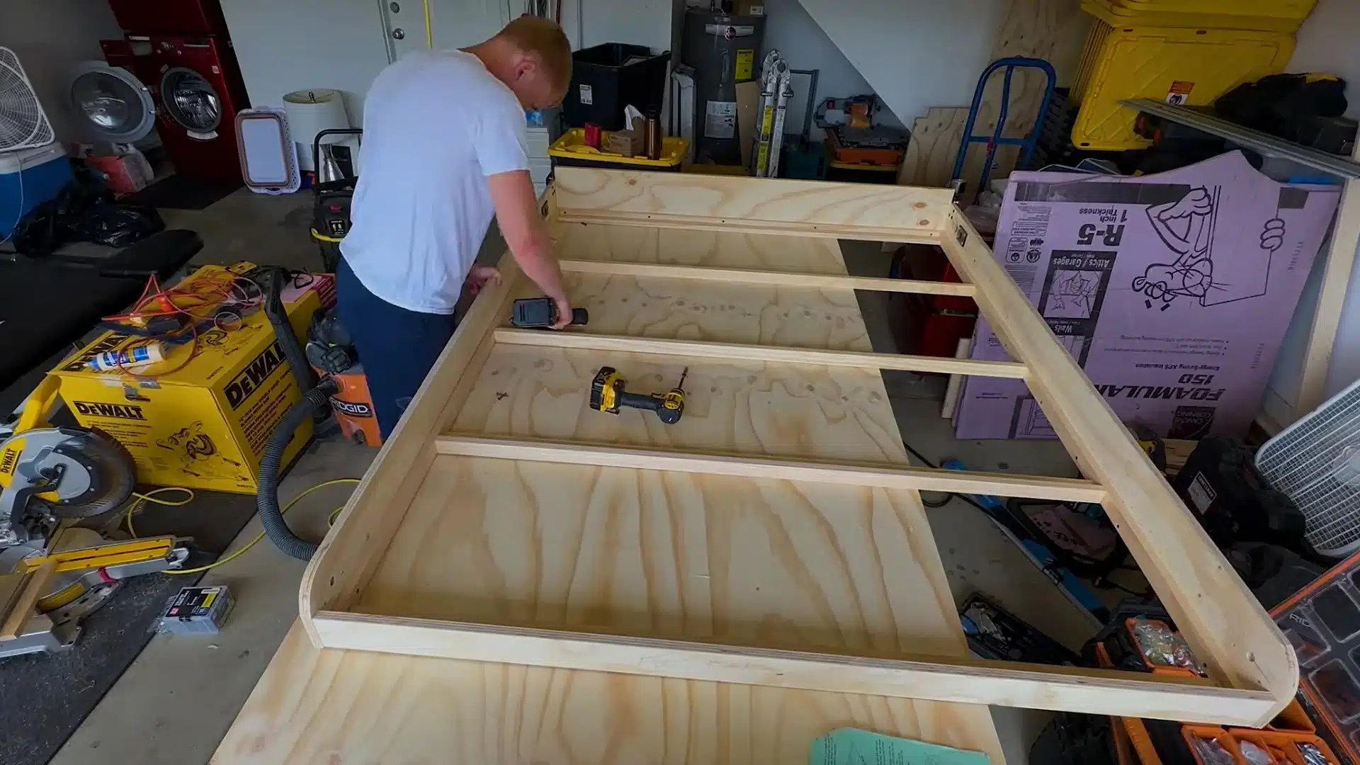man driving screws into a wooden bed frame laid across the garage workshop floor